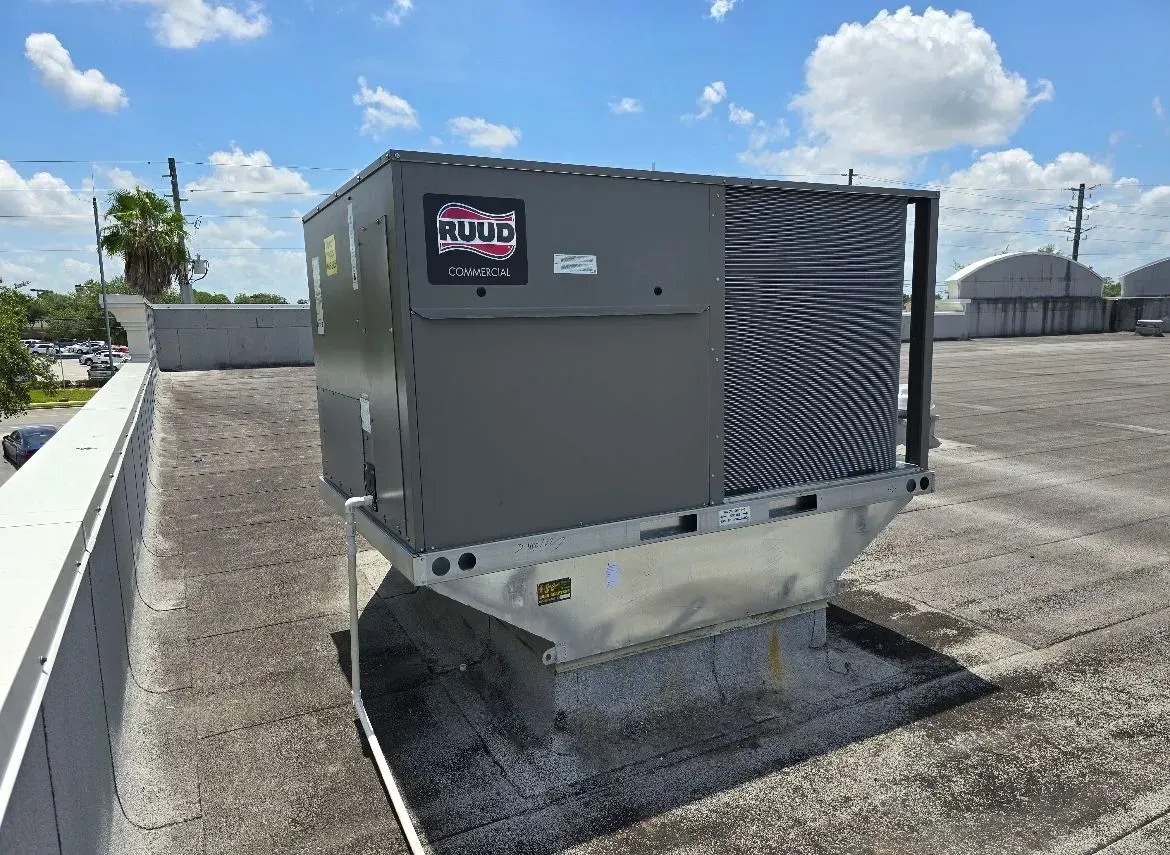 Gray rooftop HVAC unit on a gravel roof under a blue sky with clouds.