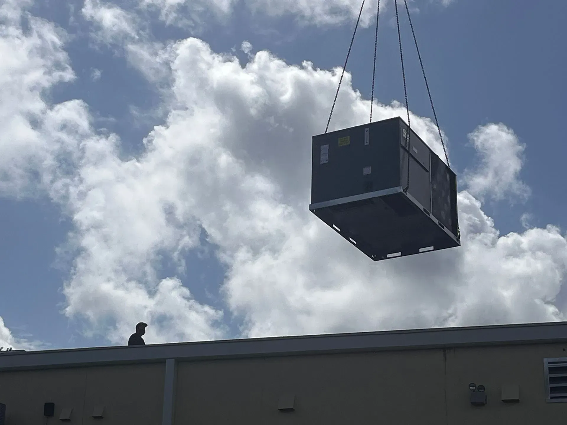 Large black crate suspended by cables above a building under a cloudy sky