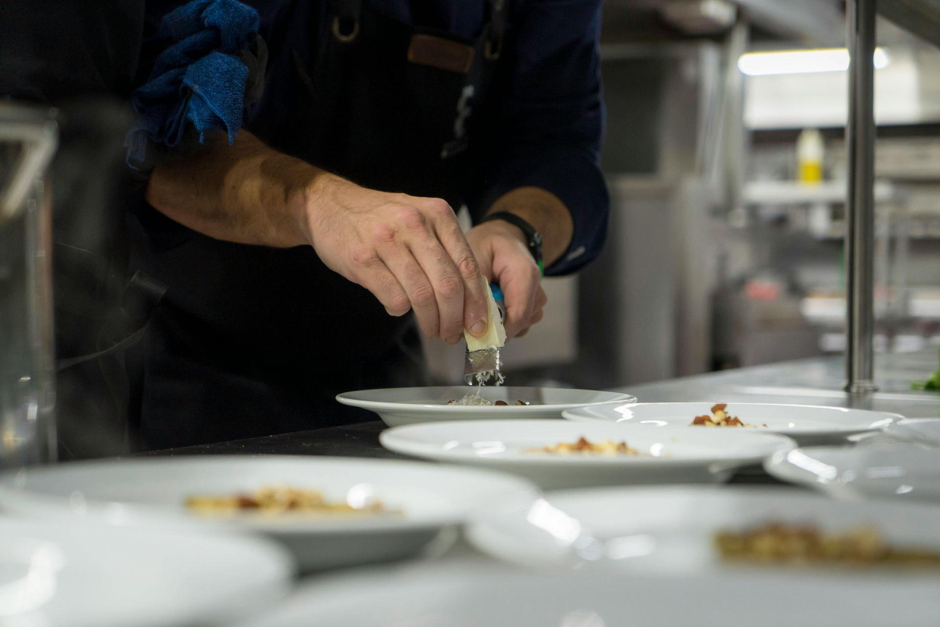 Person seasoning plated food in a kitchen with several white dishes on the counter