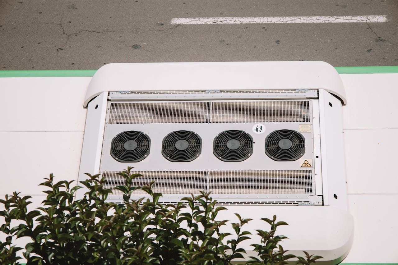 Four outdoor air conditioning units on a white rooftop beside a road.