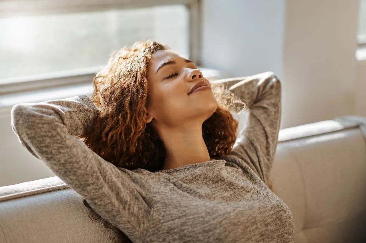 Relaxing person leaning back on a sofa with eyes closed in a sunlit living room