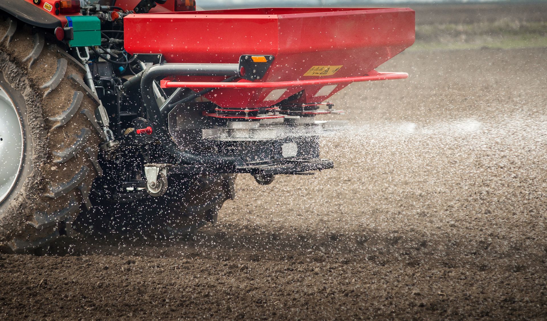 A tractor spreading fertilizer over a brown, plowed field.