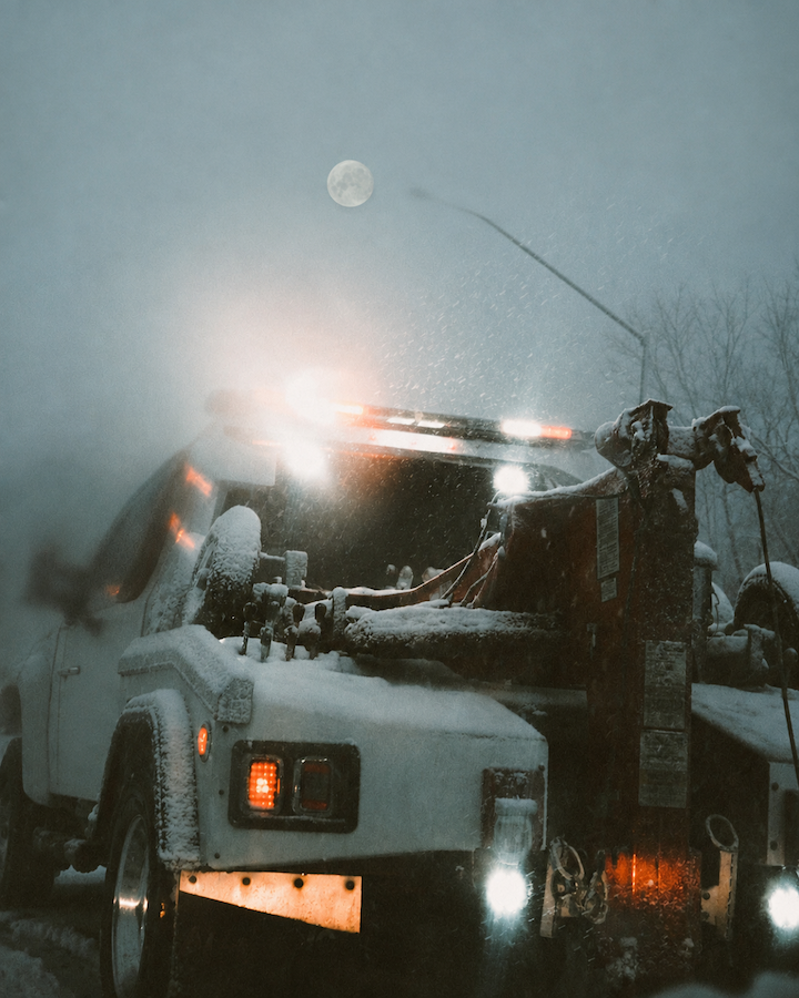 white tow truck driving through a snow storm