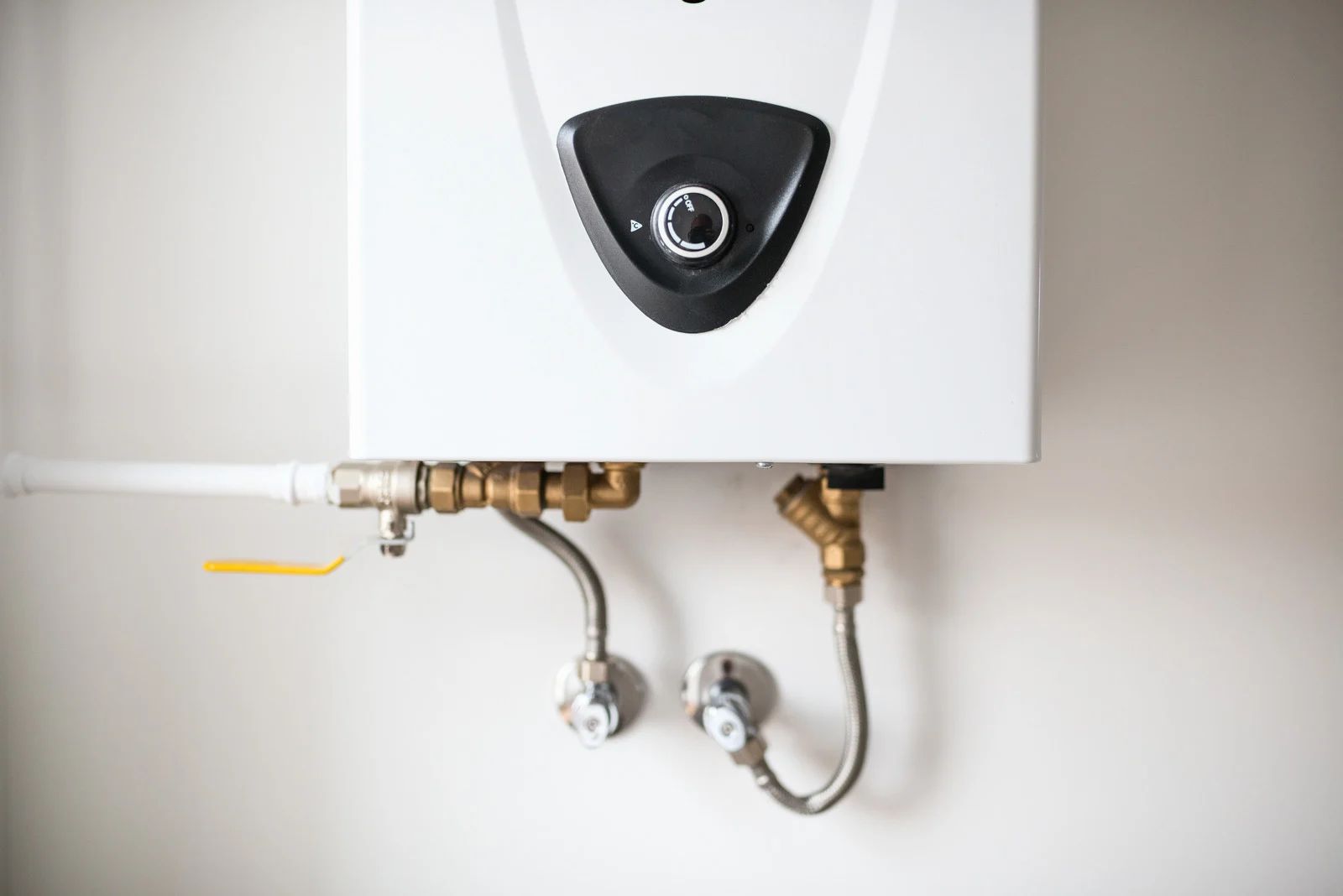 Wall-mounted white water heater with exposed pipes and valves against a plain wall