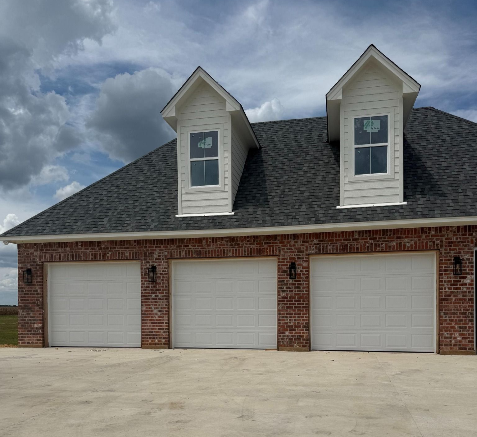 Brick garage with three bays, dark roof, two dormers, and white garage doors.