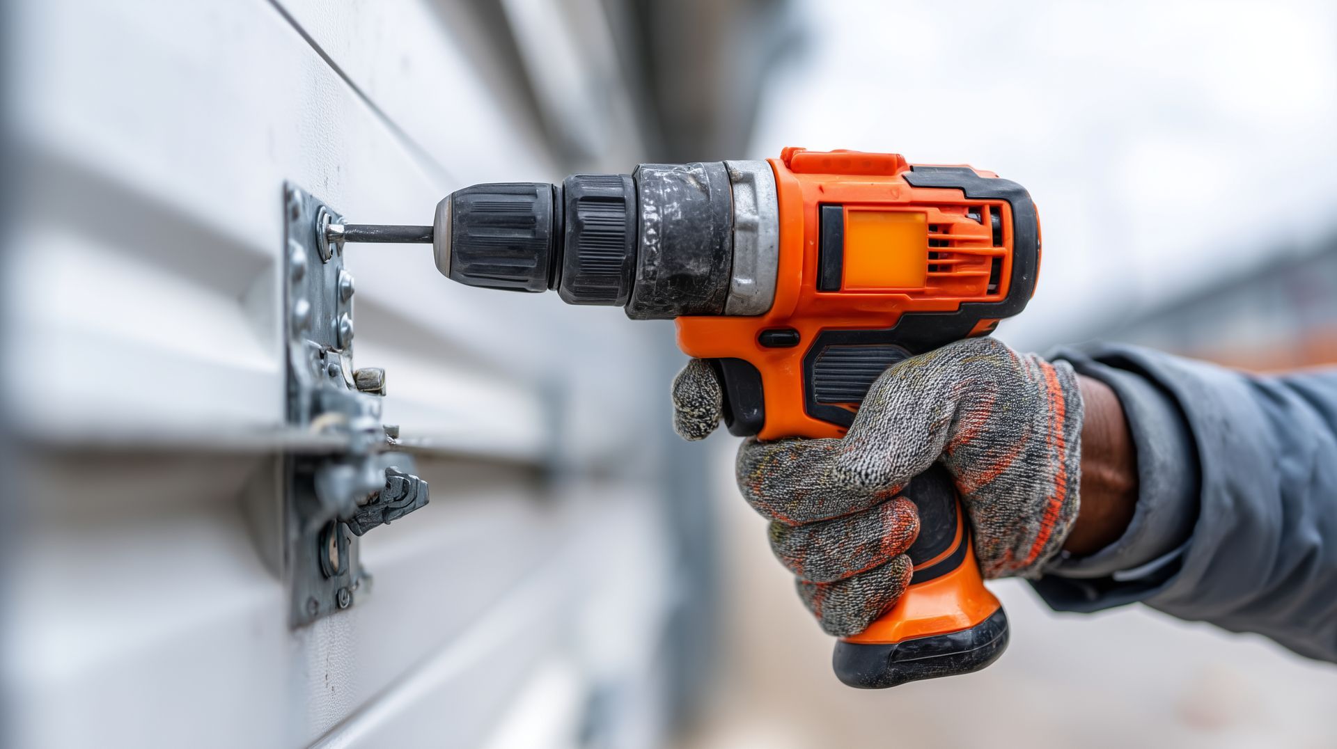 Technician replacing garage door panels after damage. A person using an orange drill to attach a metal bracket to a white surface.