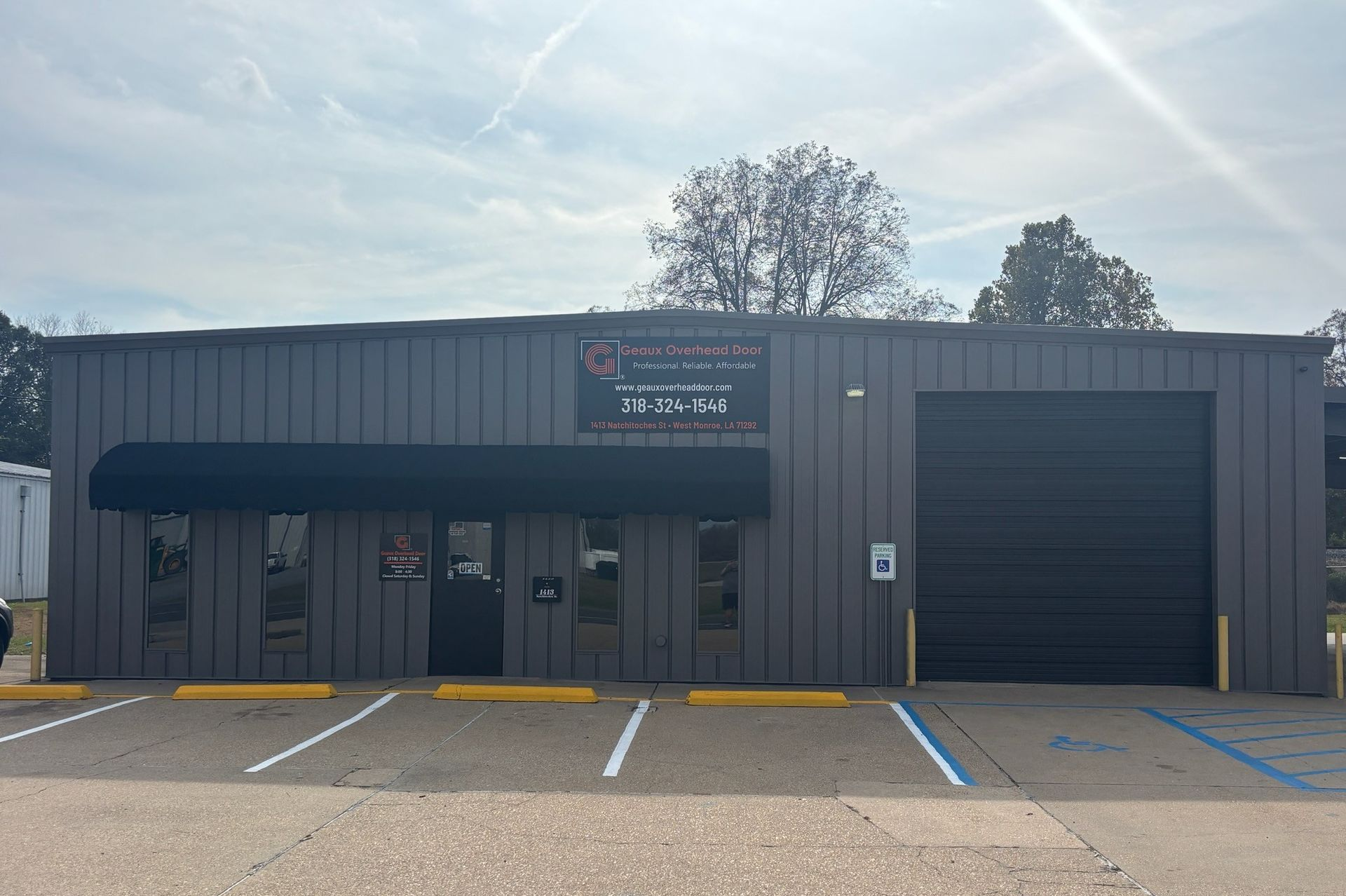 Gray commercial building with a black awning and roll-up door; parking spaces marked in white and blue.