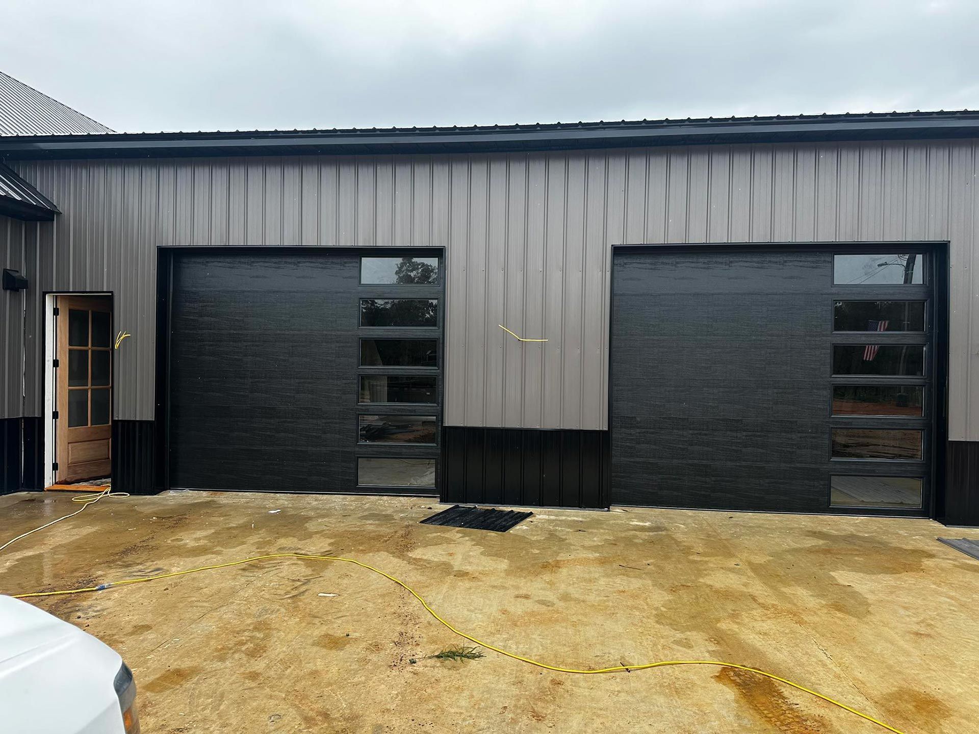 Exterior of a building with two black garage doors with windows and a side door open.