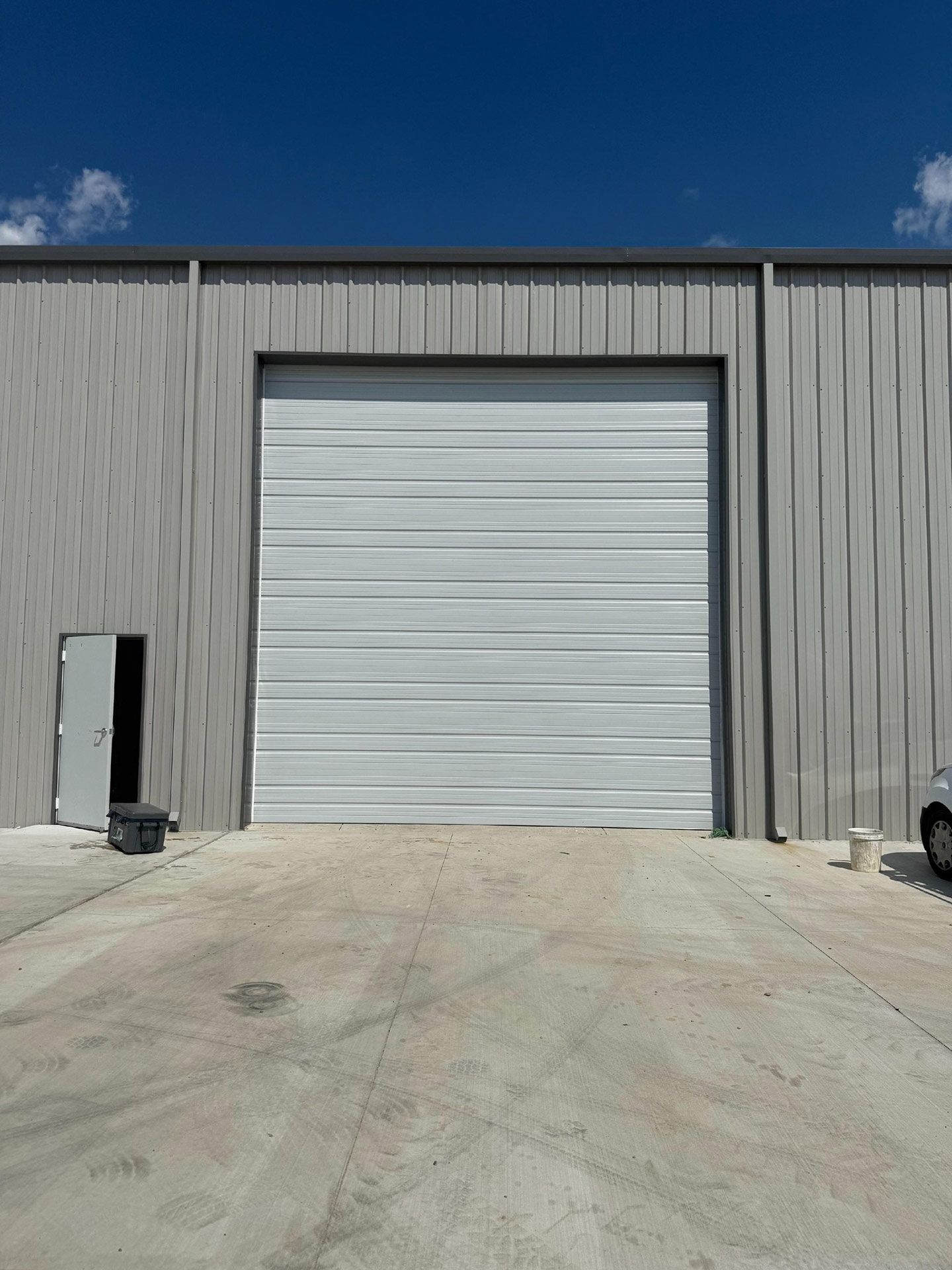 Gray industrial building with closed garage door and open side door, blue sky overhead.