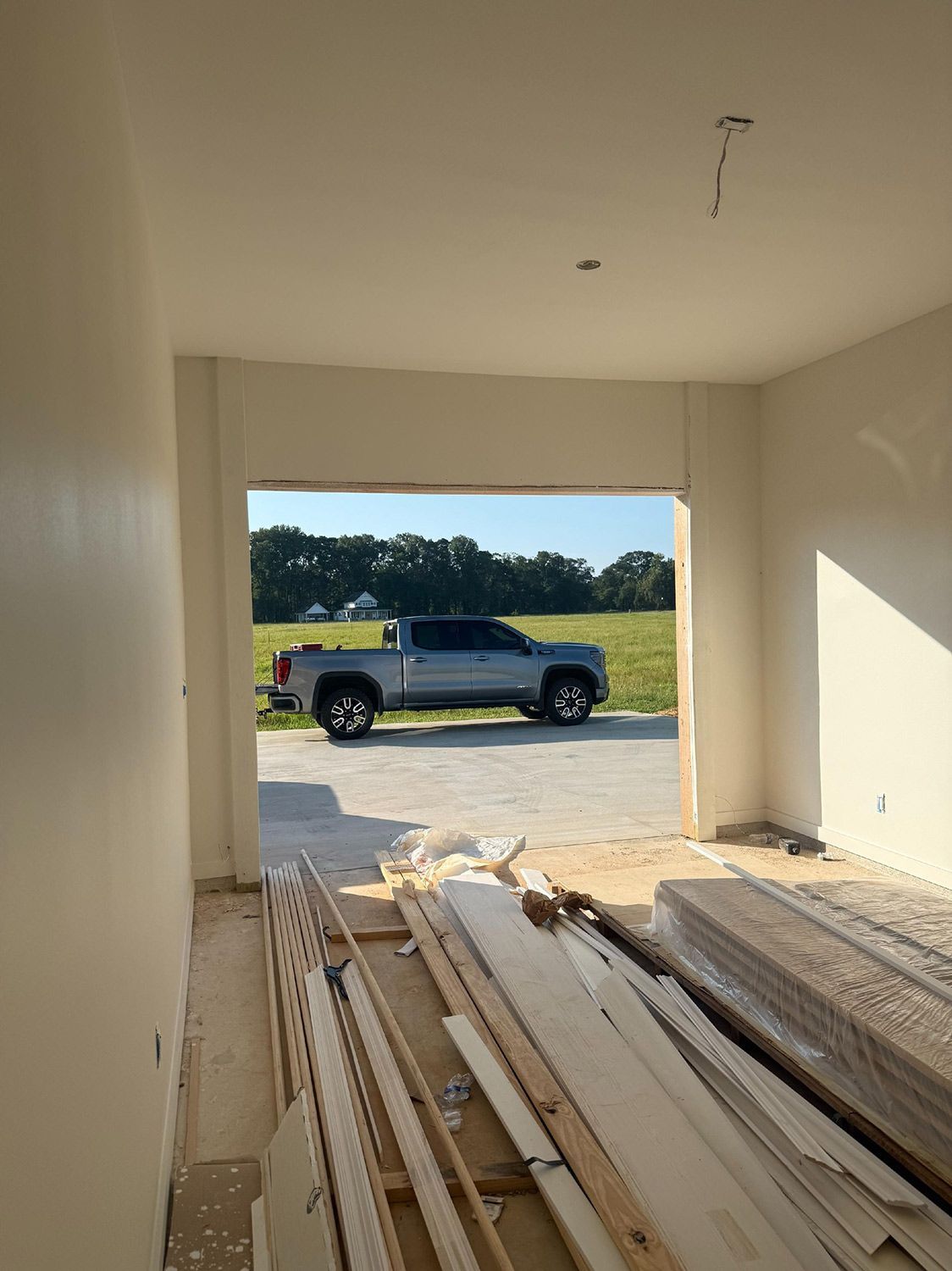 Interior view of a building under construction, looking out at a gray pickup truck on a grassy field.