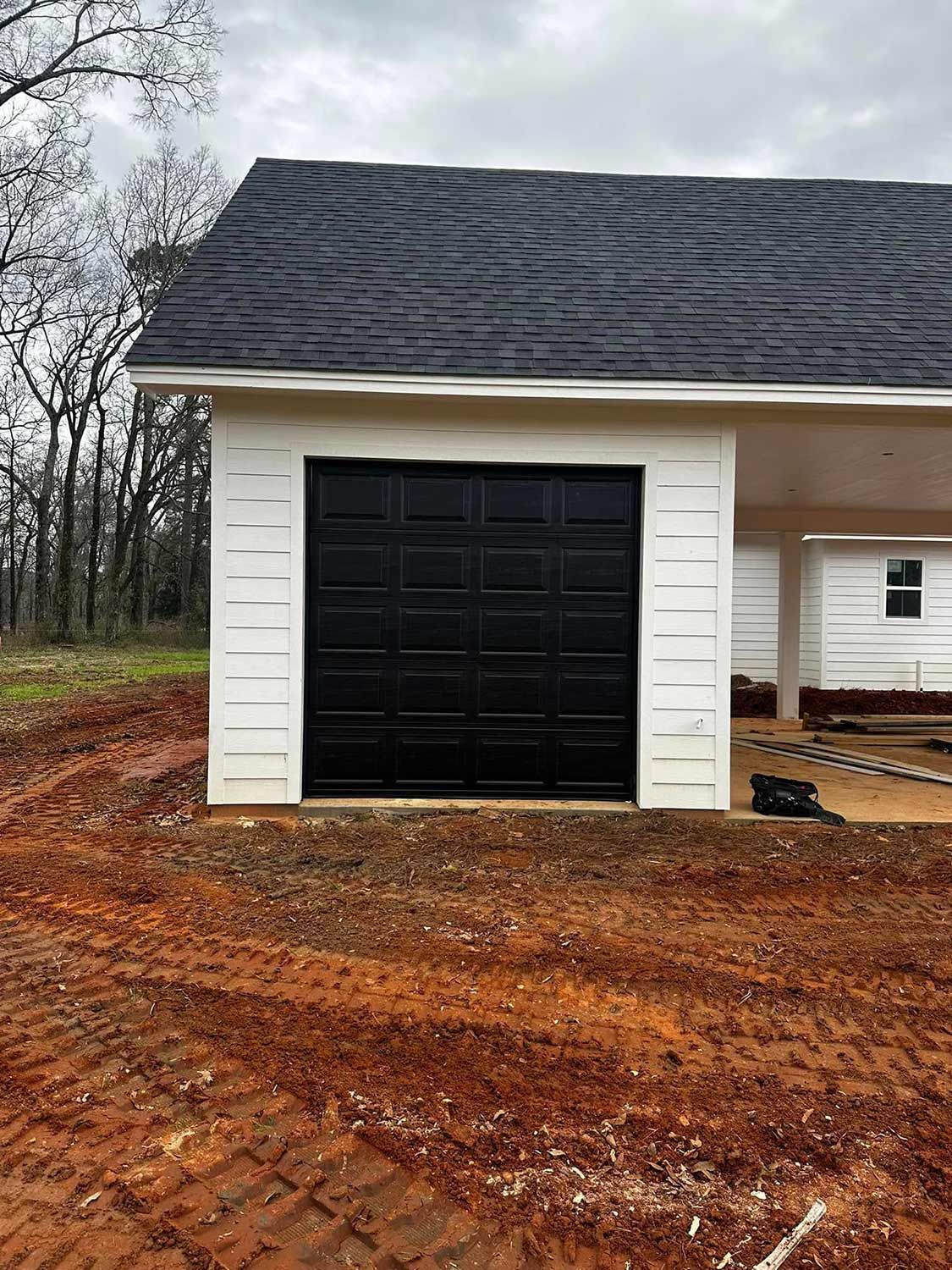 Black garage door on a white building with black roof; brown earth and overcast sky.