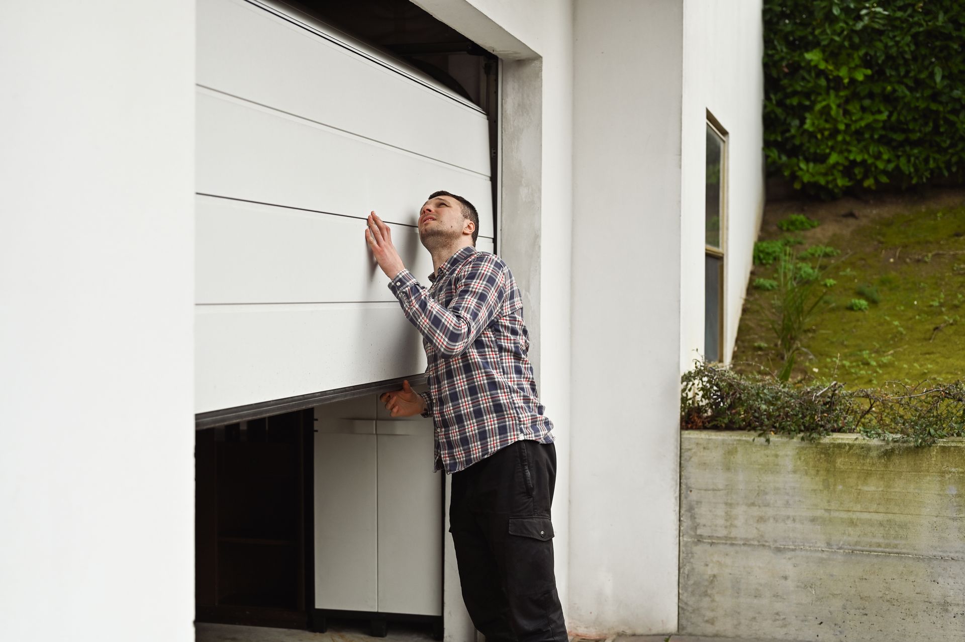 Man checking the partially open white garage door, outdoors.