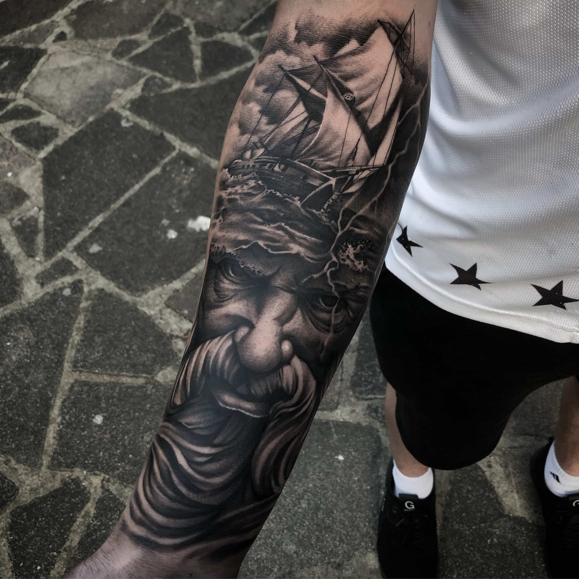 Tattoo of a bearded man with ship sailing in a storm on arm. Black and gray shading.