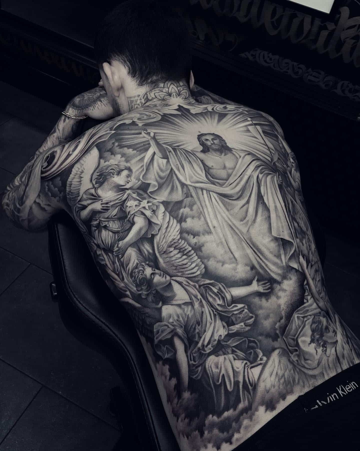 Full back tattoo of Jesus ascending to heaven, surrounded by angels and clouds. Black and grey.
