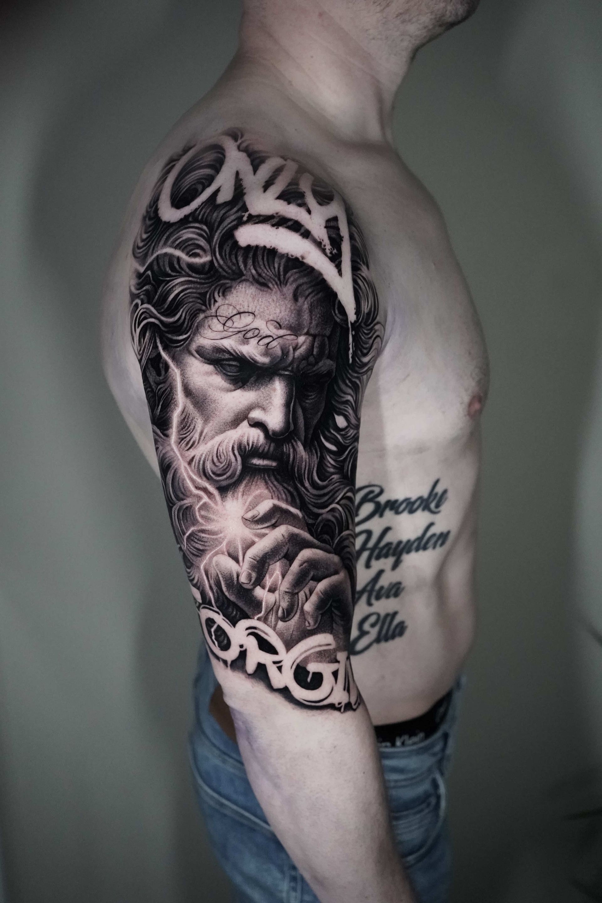 Man's arm with detailed black and white tattoo of a bearded man with a crown; names on torso.