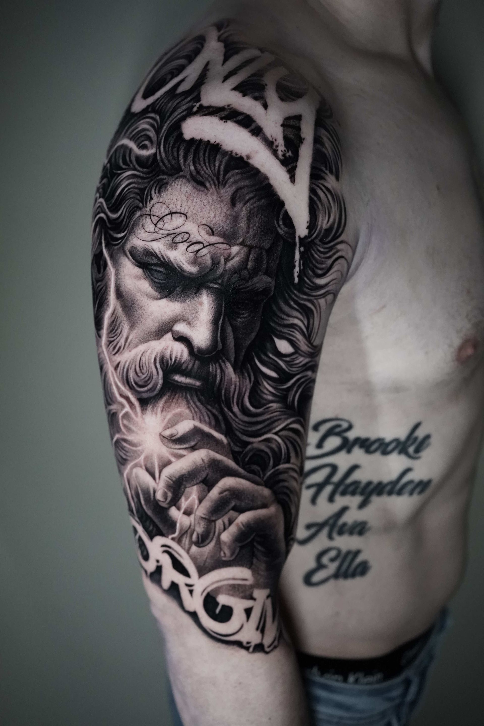 Tattoo of a bearded face on a man's arm, with graffiti-style text at the top and bottom.