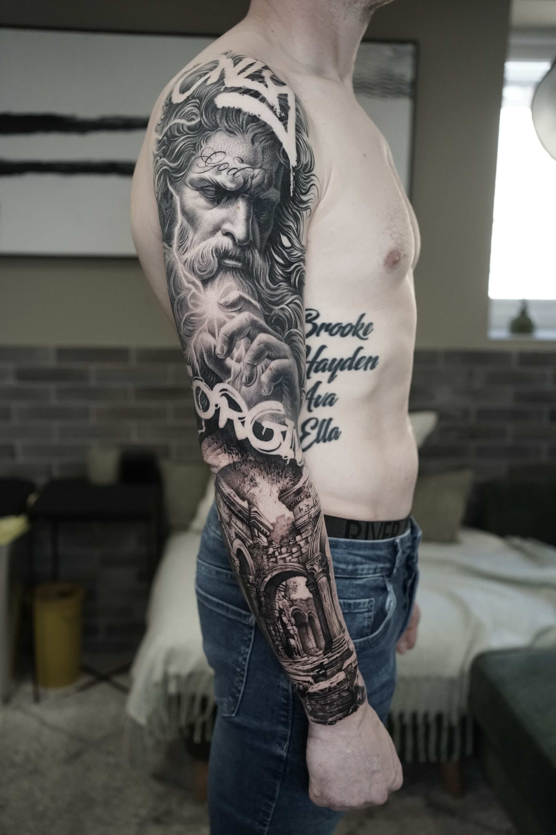 Man with full-sleeve tattoo featuring a portrait, cloudy sky, and architectural elements.