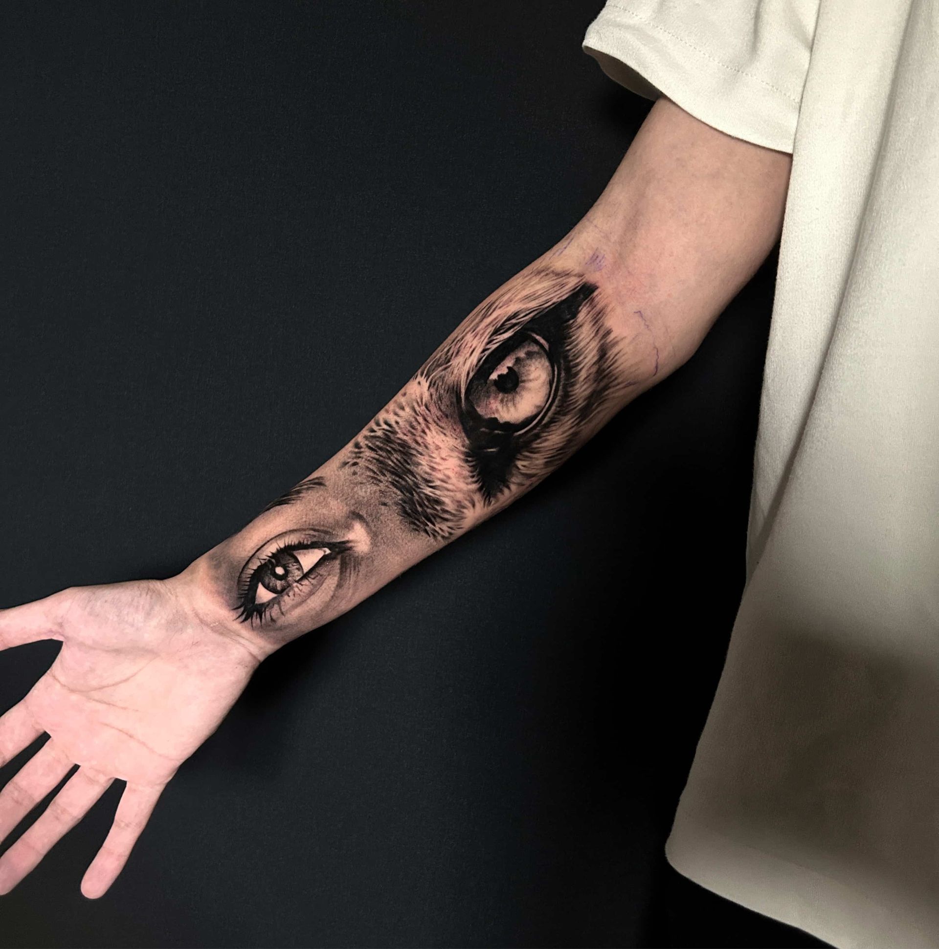Black and gray tattoo of animal eyes on a person's forearm. One eye near the wrist, the other higher up.