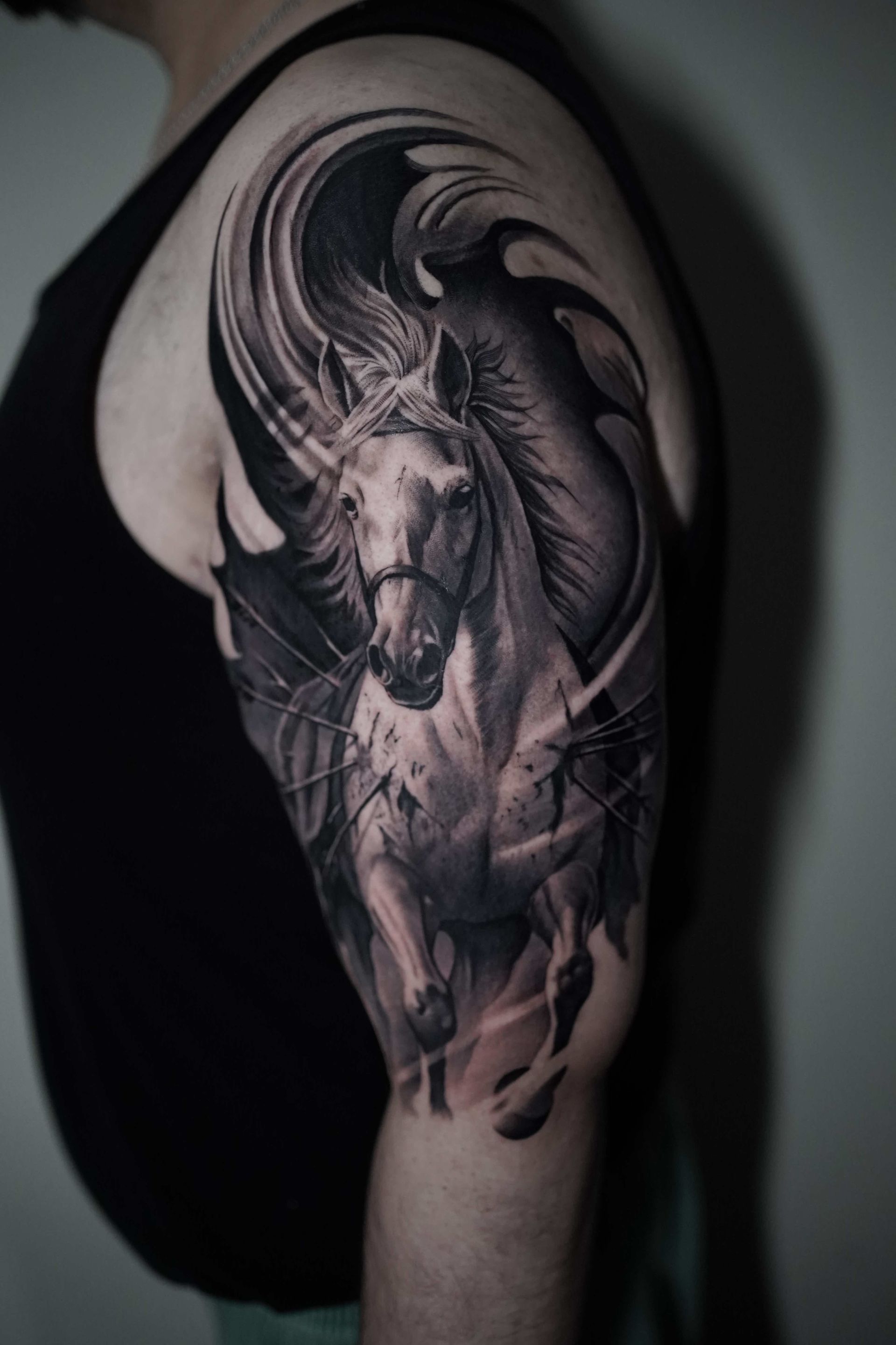 Black and white tattoo of a horse with wings on a person's upper arm.
