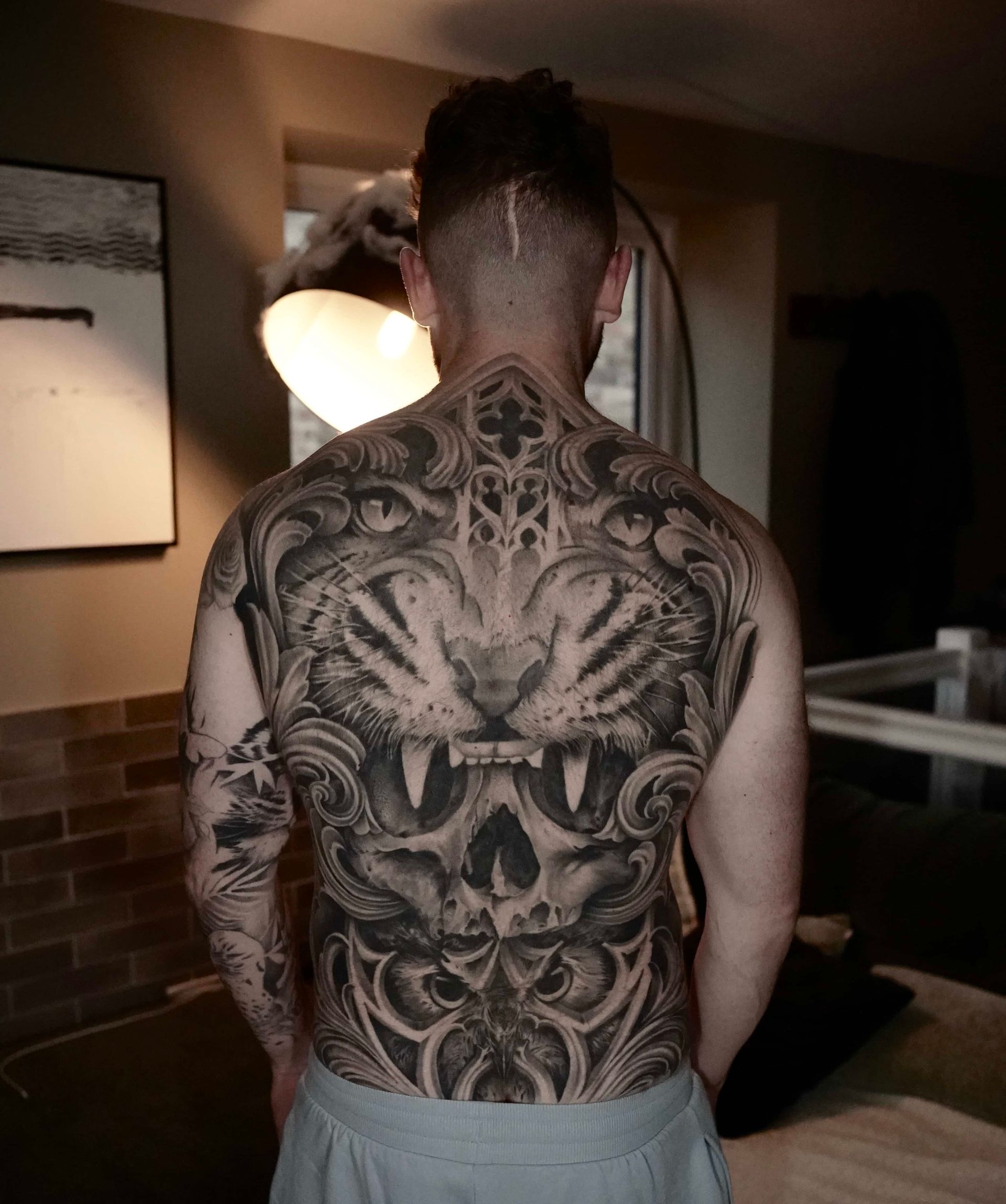 Man with elaborate tiger-themed back tattoo; torso visible, indoors.