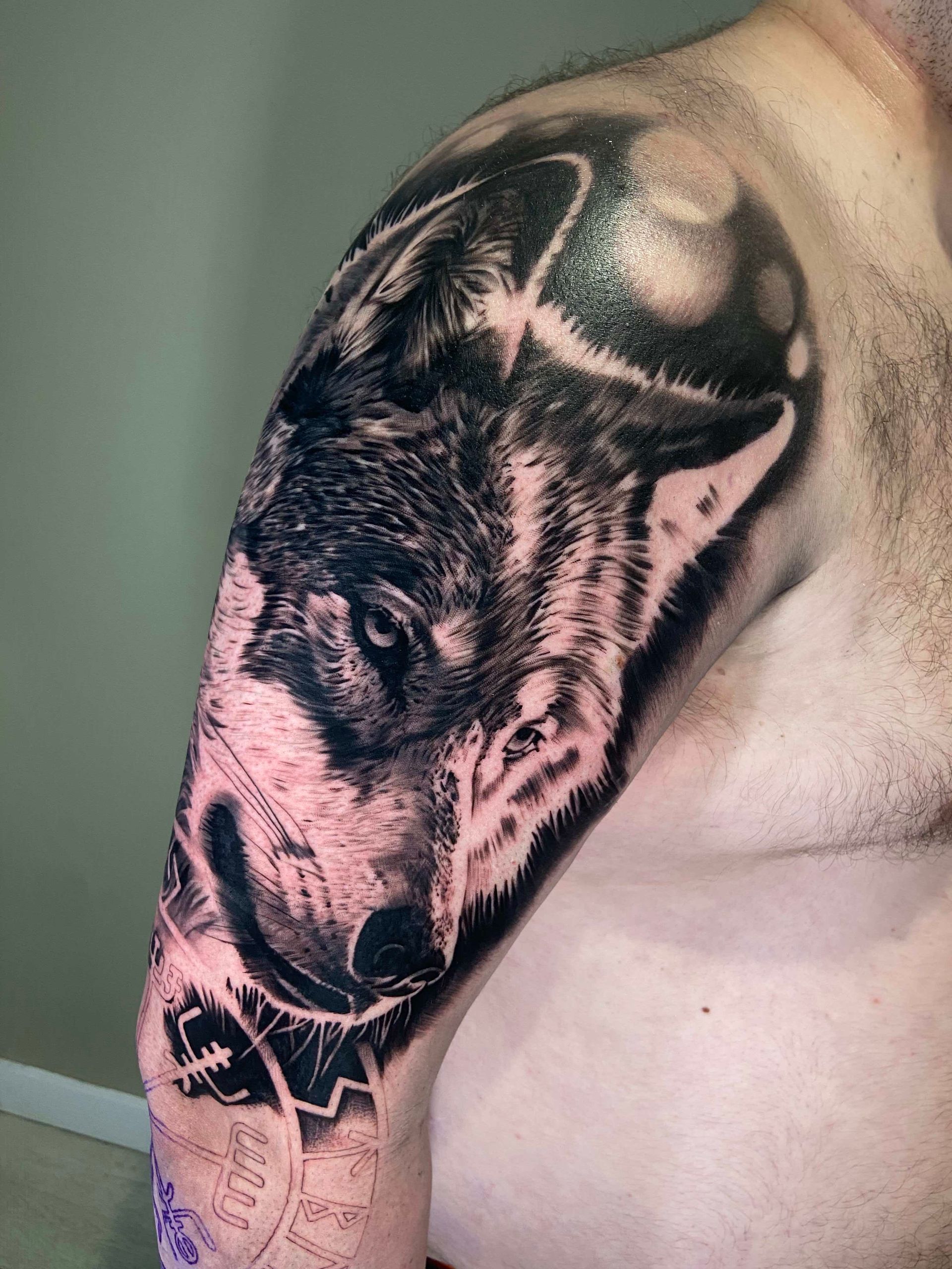 Black and gray wolf tattoo on a person's upper arm and shoulder.