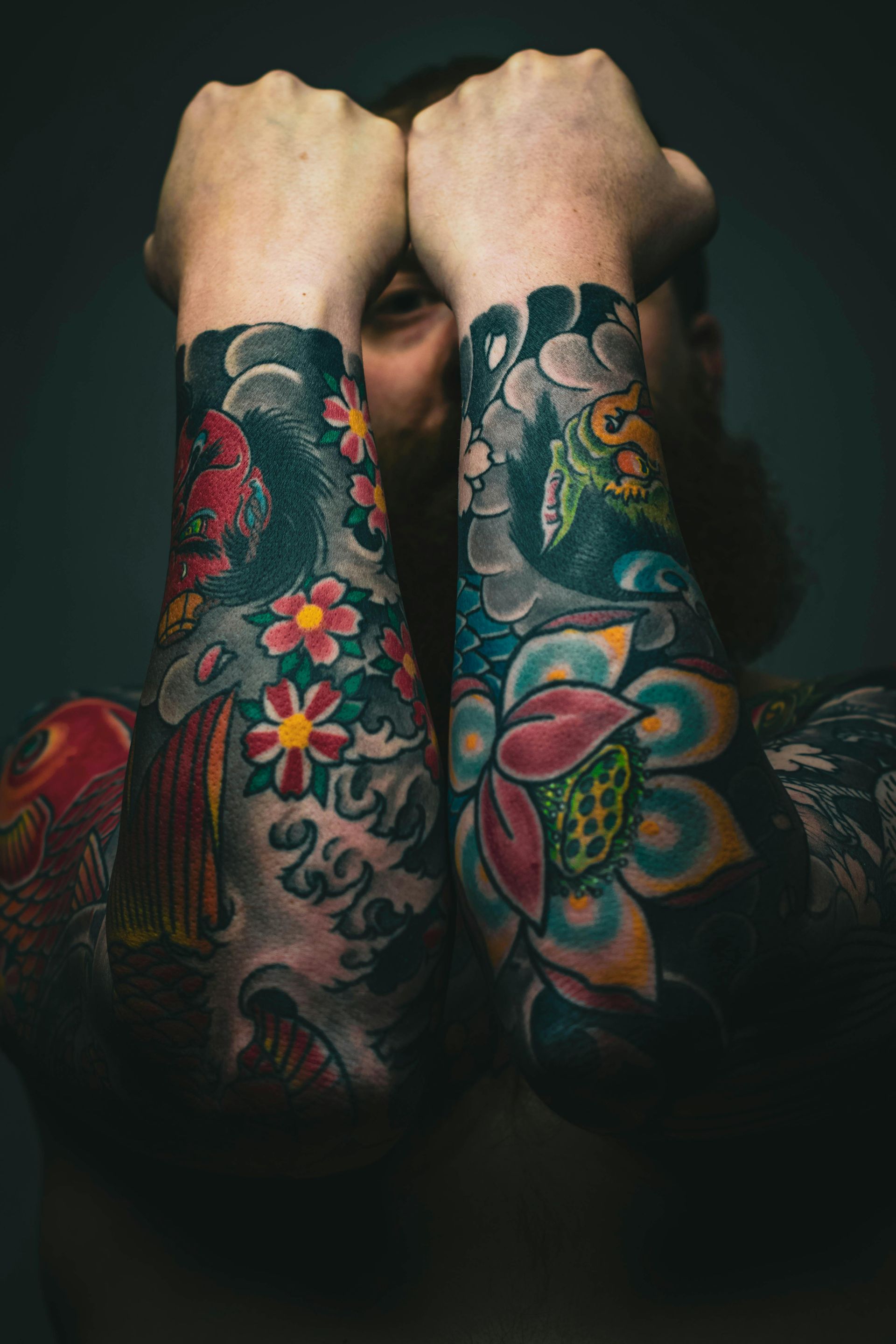 Person with full arm sleeve tattoos covering their arms, holding them up to face; vibrant colors.