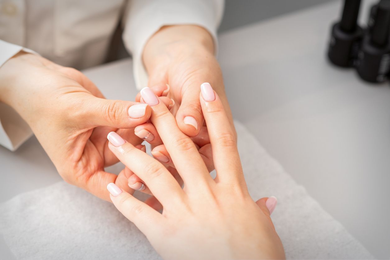 Una persona se hace la manicura. Otra persona sostiene la mano, con las uñas pintadas de rosa claro.