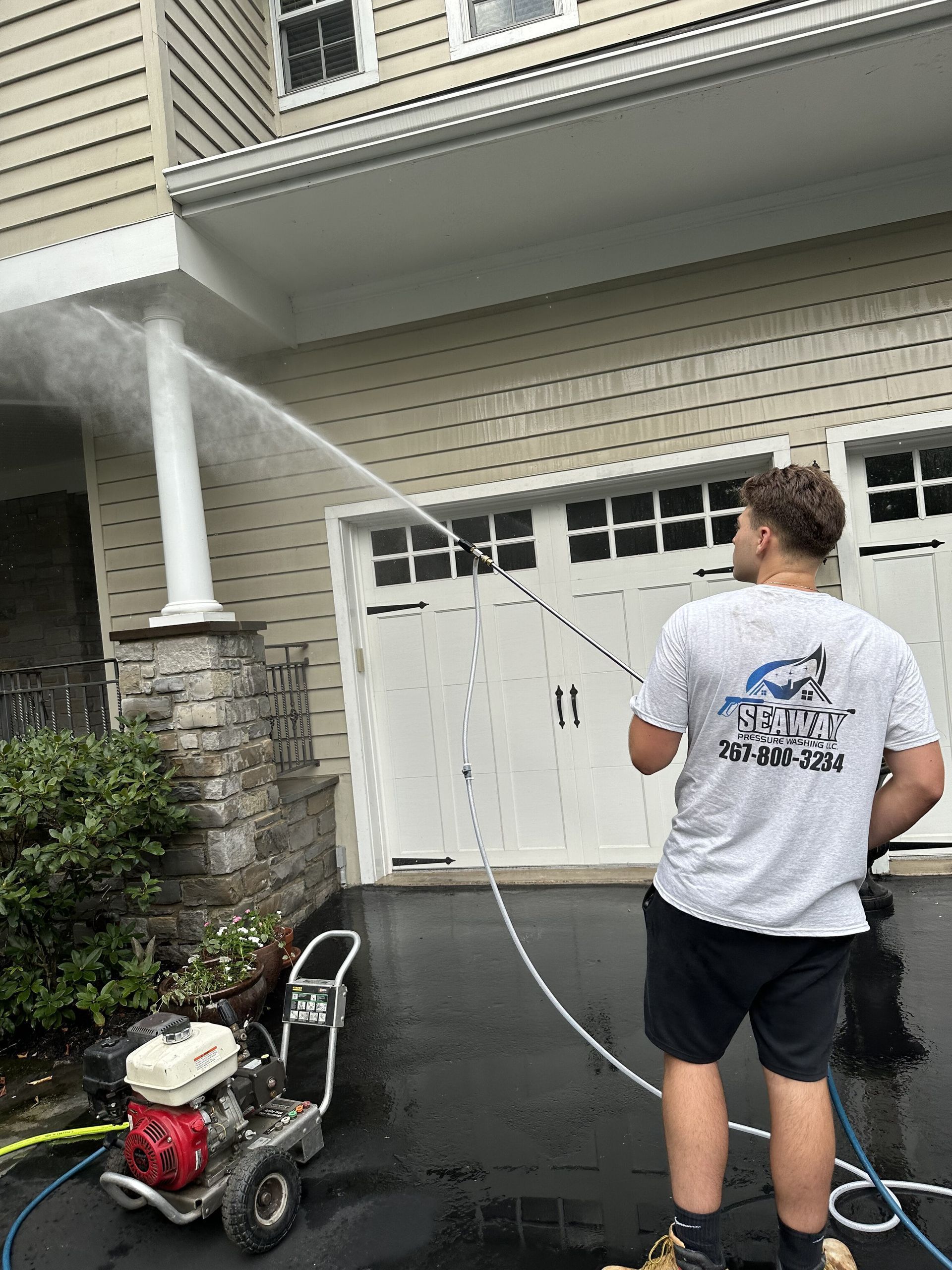 A man is using a pressure washer to clean the driveway of a house.