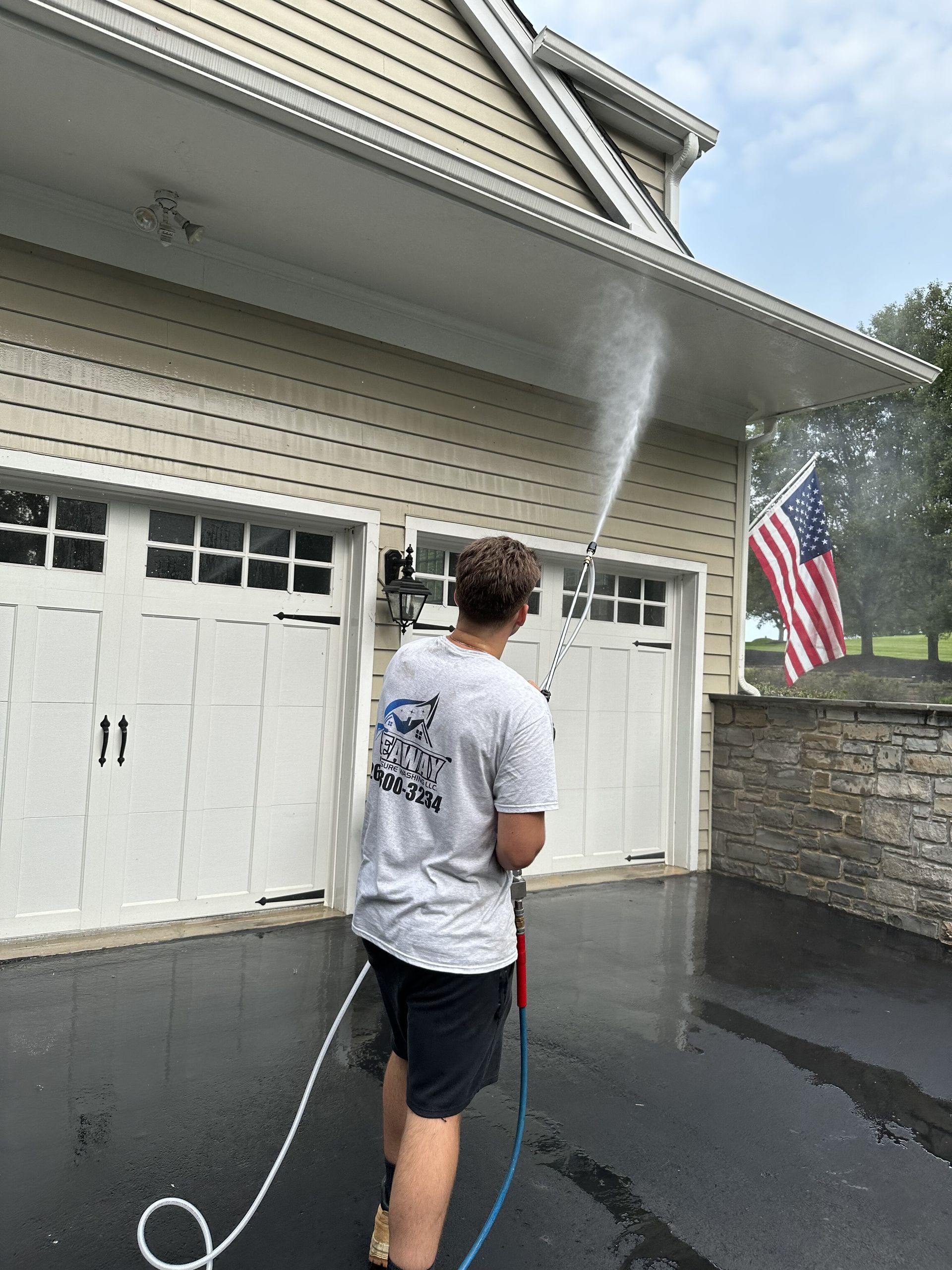 A man is cleaning the side of a house with a pressure washer.
