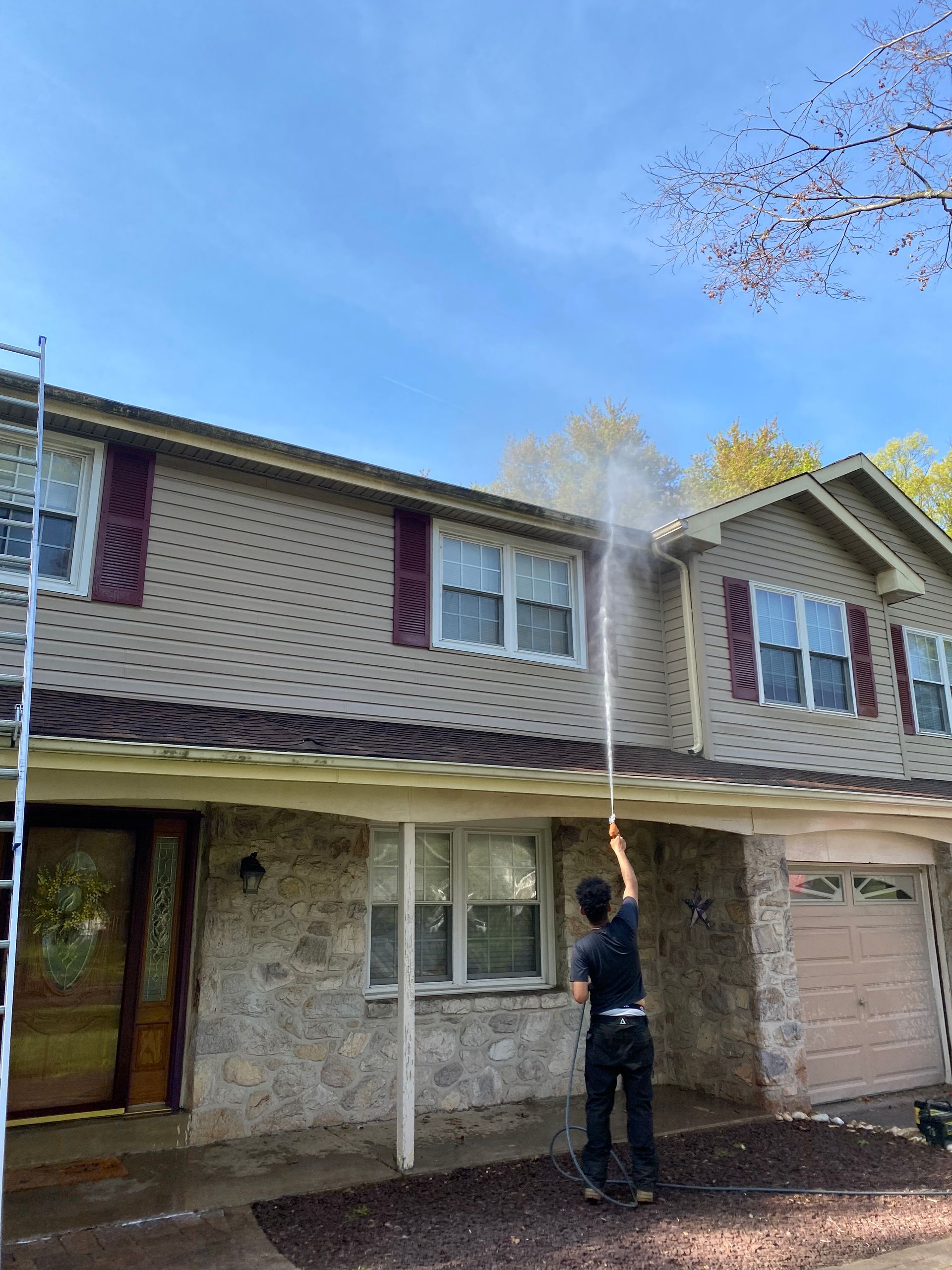 A man is cleaning the roof of a house with a pressure washer.
