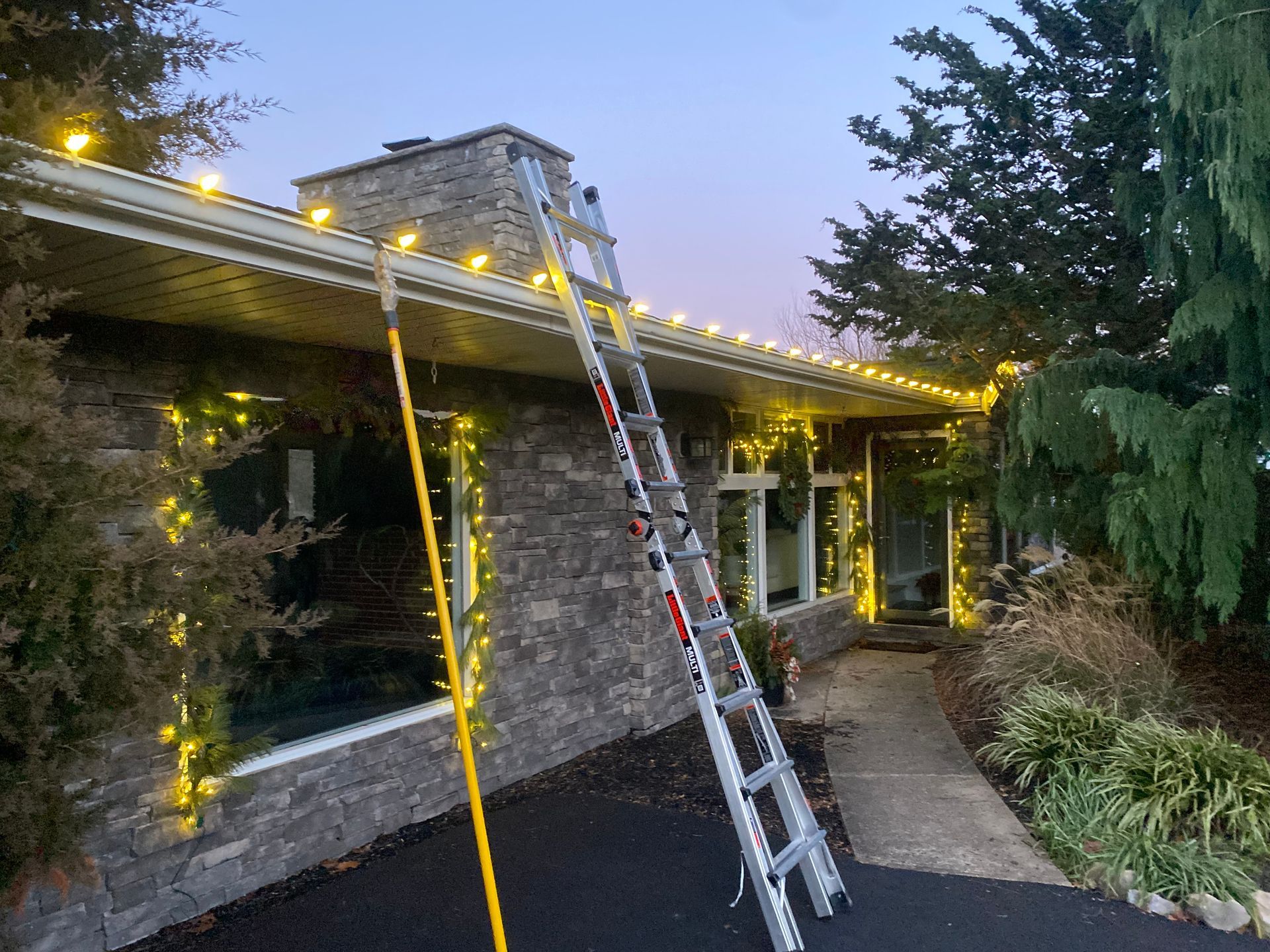 A ladder is sitting in front of a house decorated with christmas lights.