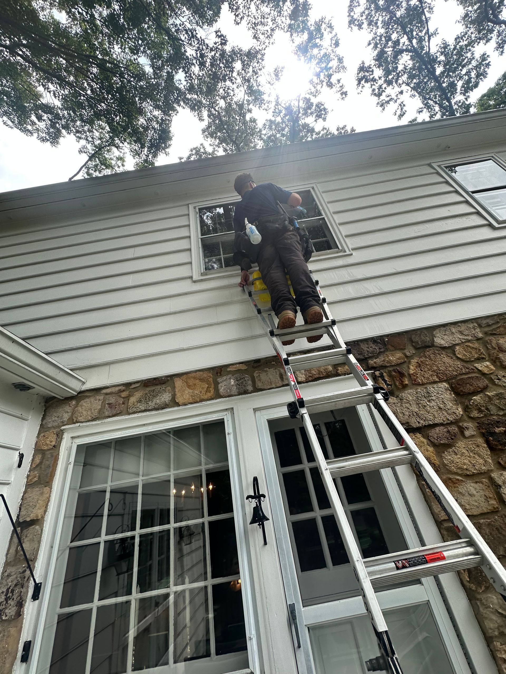 A man is standing on a ladder on the side of a house.