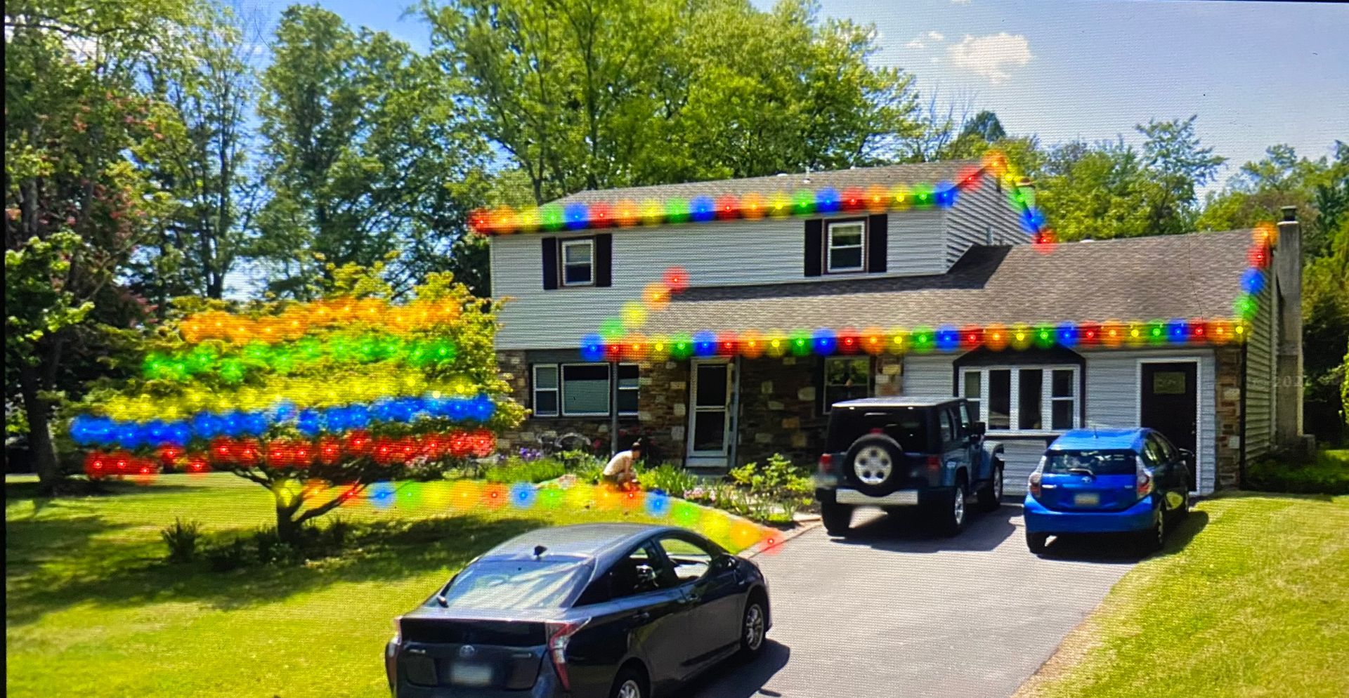 A car is parked in front of a house with christmas lights on the roof.