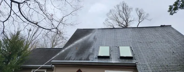 A person is cleaning the roof of a house with a soft wash machine.