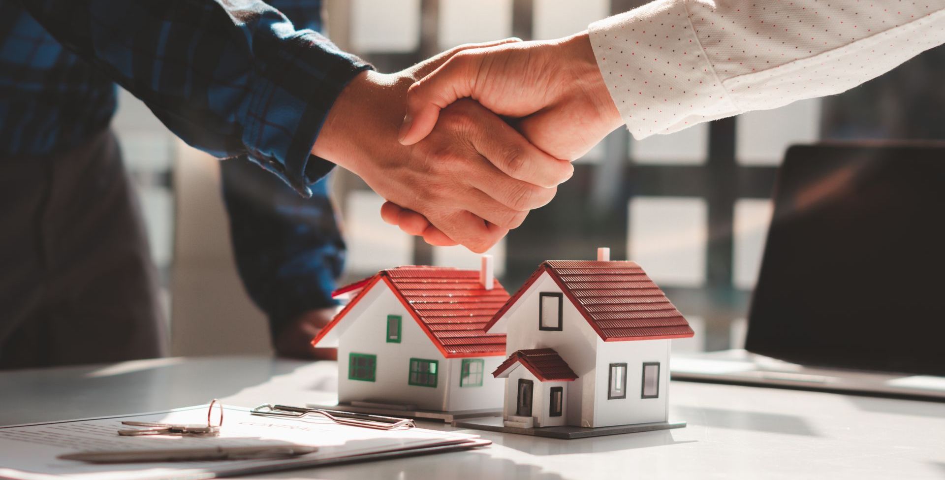 Two people are shaking hands over a table with two small houses.