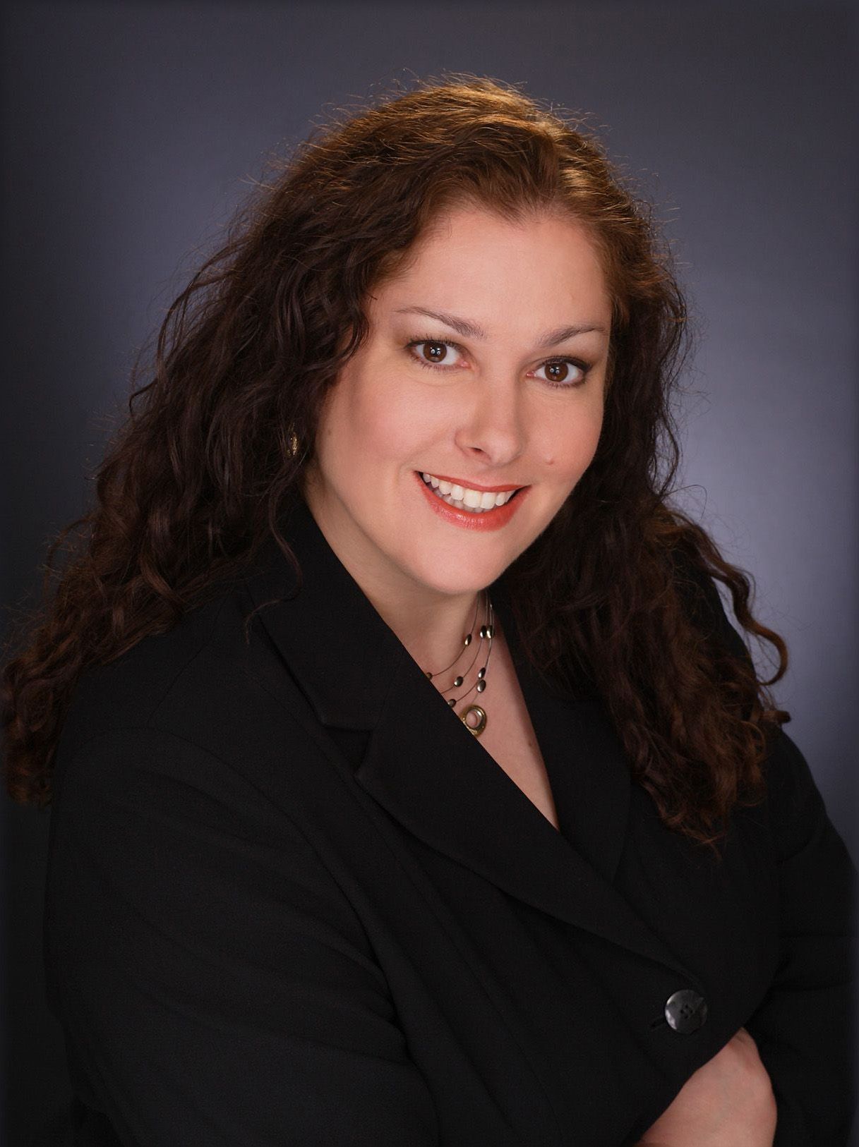 A woman in a black jacket and necklace is smiling for the camera.