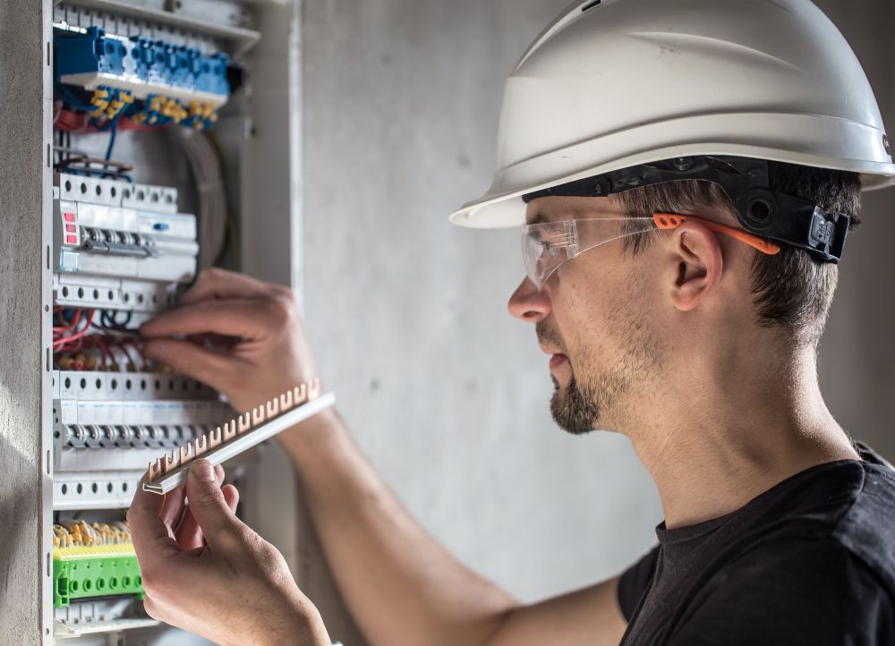 A man wearing a hard hat and safety glasses is working on an electrical box.