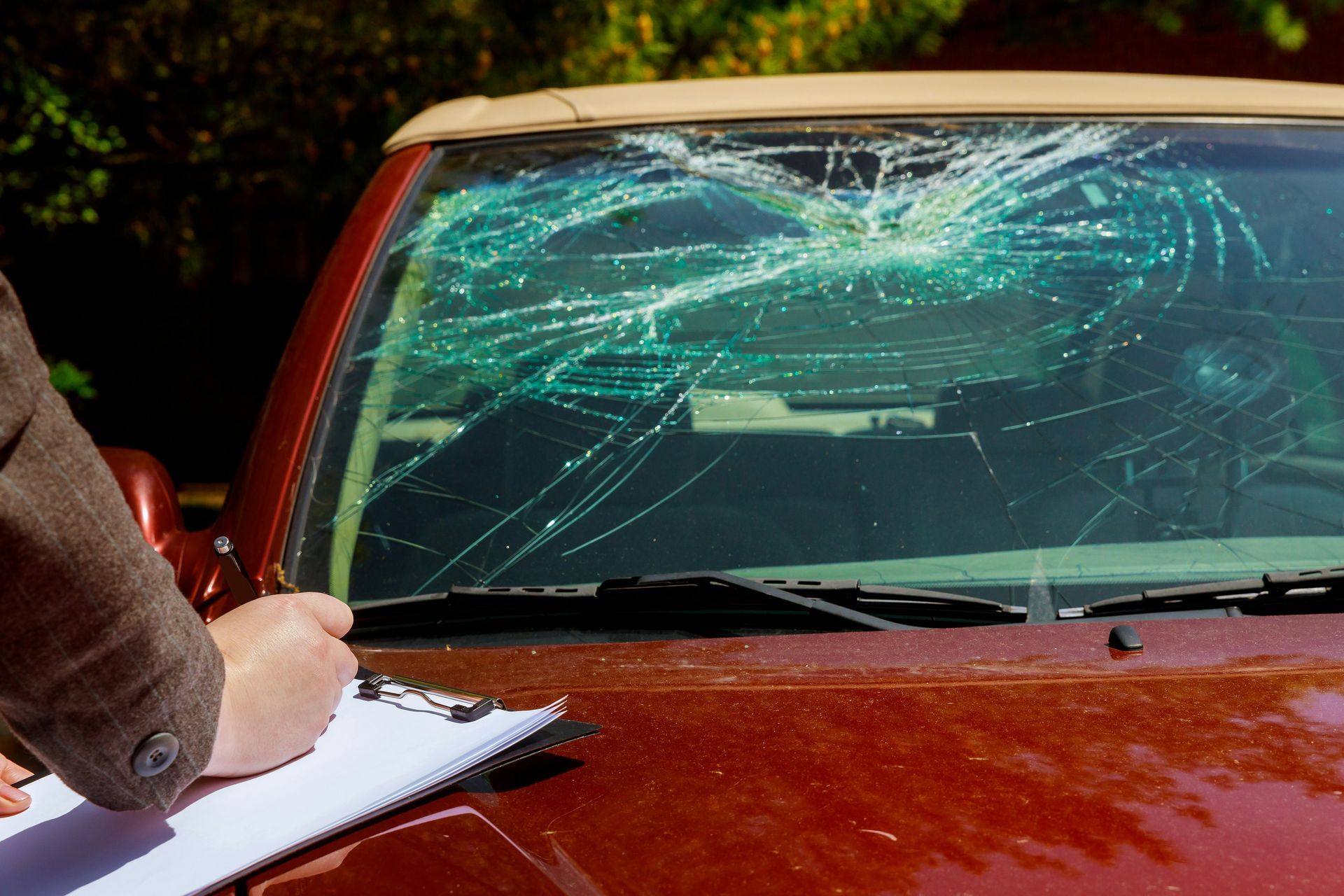 A person is writing on a clipboard next to a car with a broken windshield