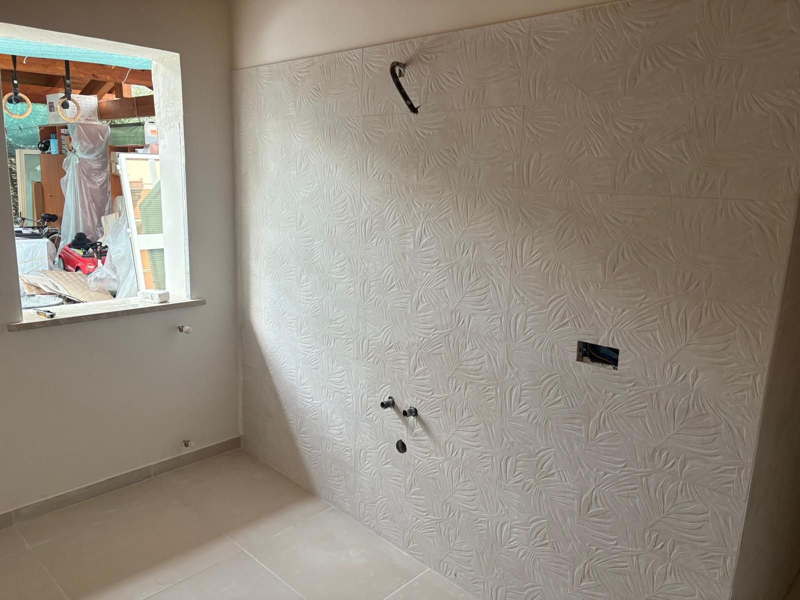 Stanza vuota con parete ruvida, cavi elettrici a vista e finestra che si apre su un cantiere esterno.