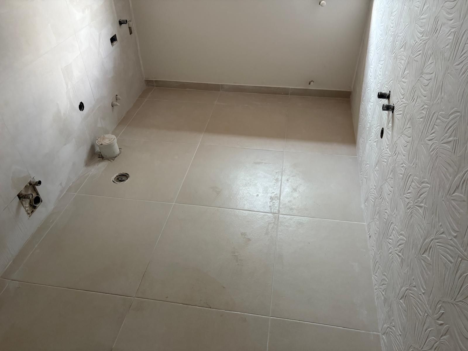 Stanza vuota piastrellata con pareti bianche e prese elettriche a vista.