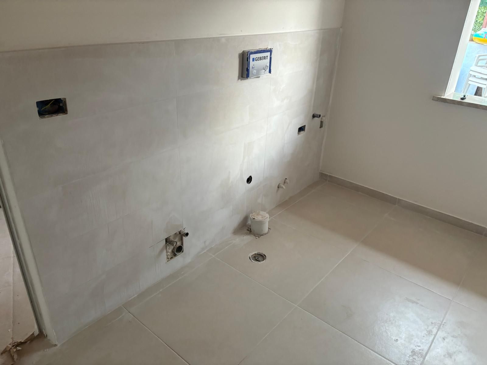 Parete vuota piastrellata del bagno o della lavanderia, con sanitari e finestra.