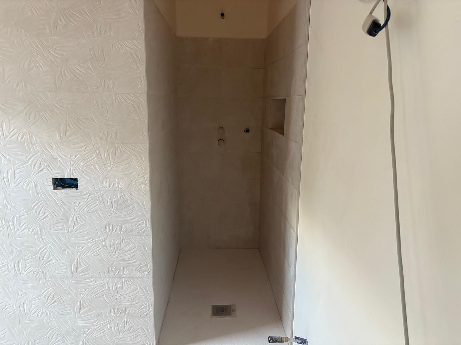 Stretto corridoio non rifinito con pareti beige, una piccola apertura nel muro e una porta in fondo.