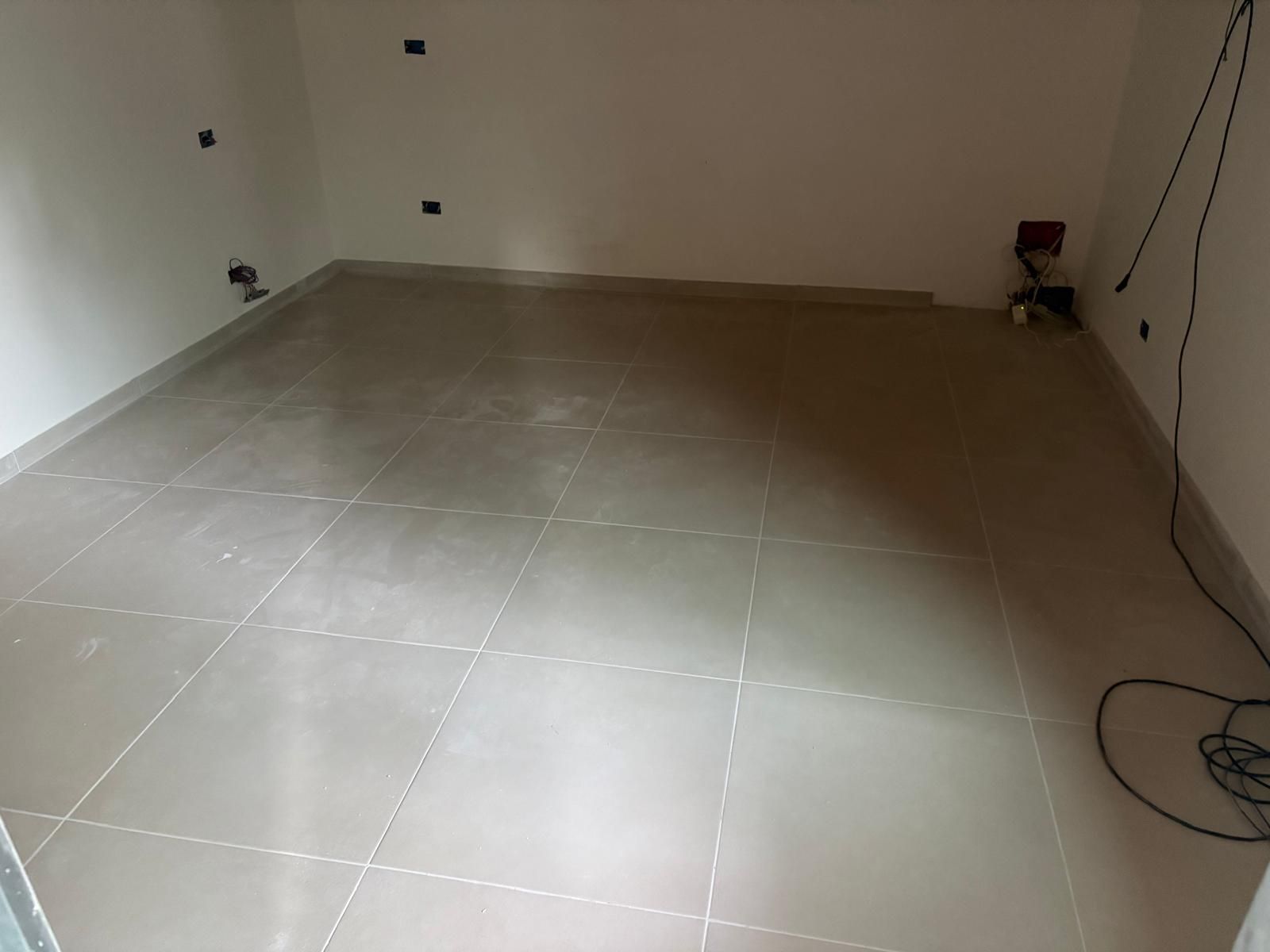Stanza vuota piastrellata con pareti bianche e un cavo sul pavimento vicino alla parete destra.