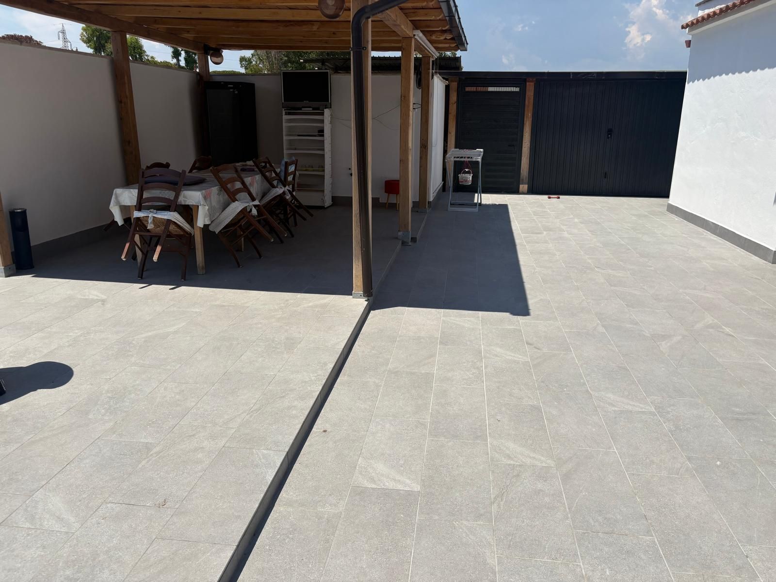Patio con pavimento piastrellato, zona salotto coperta e grande porta da garage scura in piena luce del sole
