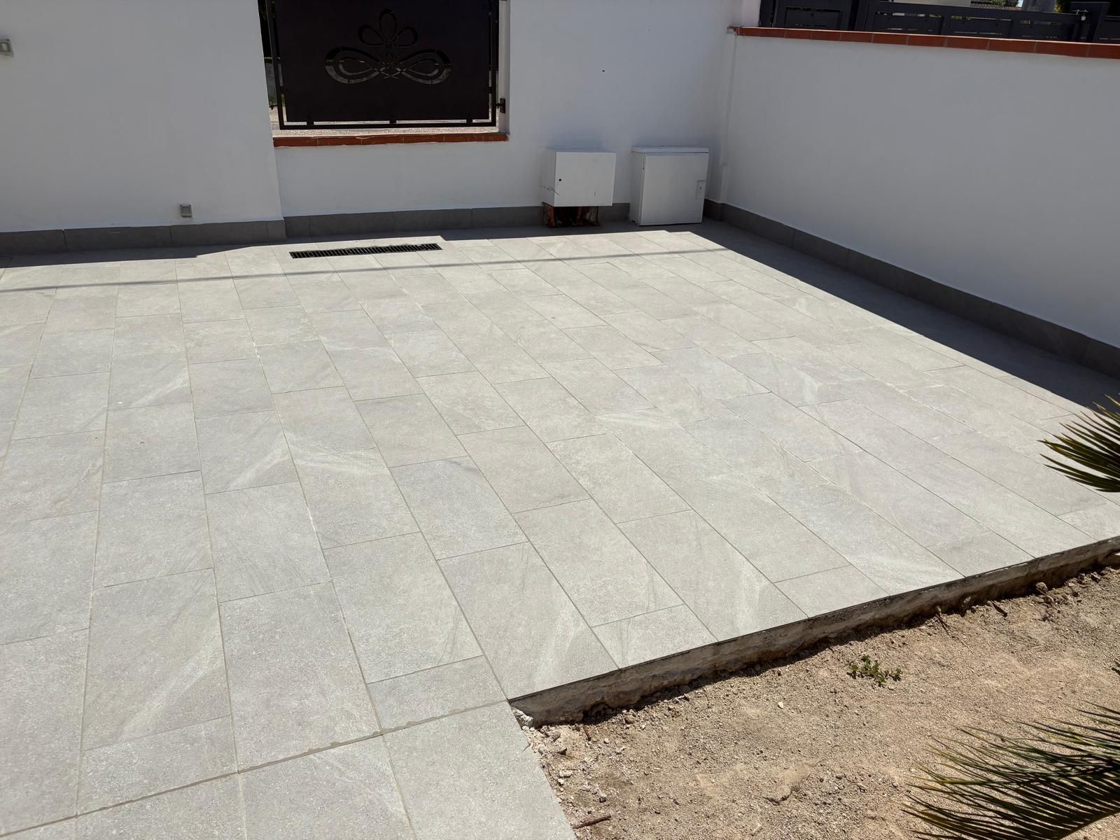 Patio piastrellato vuoto adiacente a un muro di casa, con una piccola aiuola di ghiaia in un angolo.