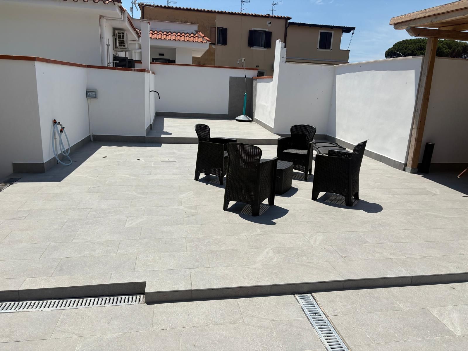 Terrazza panoramica vuota con sedie da esterno nere disposte attorno a un tavolo, sotto la luce intensa del sole.