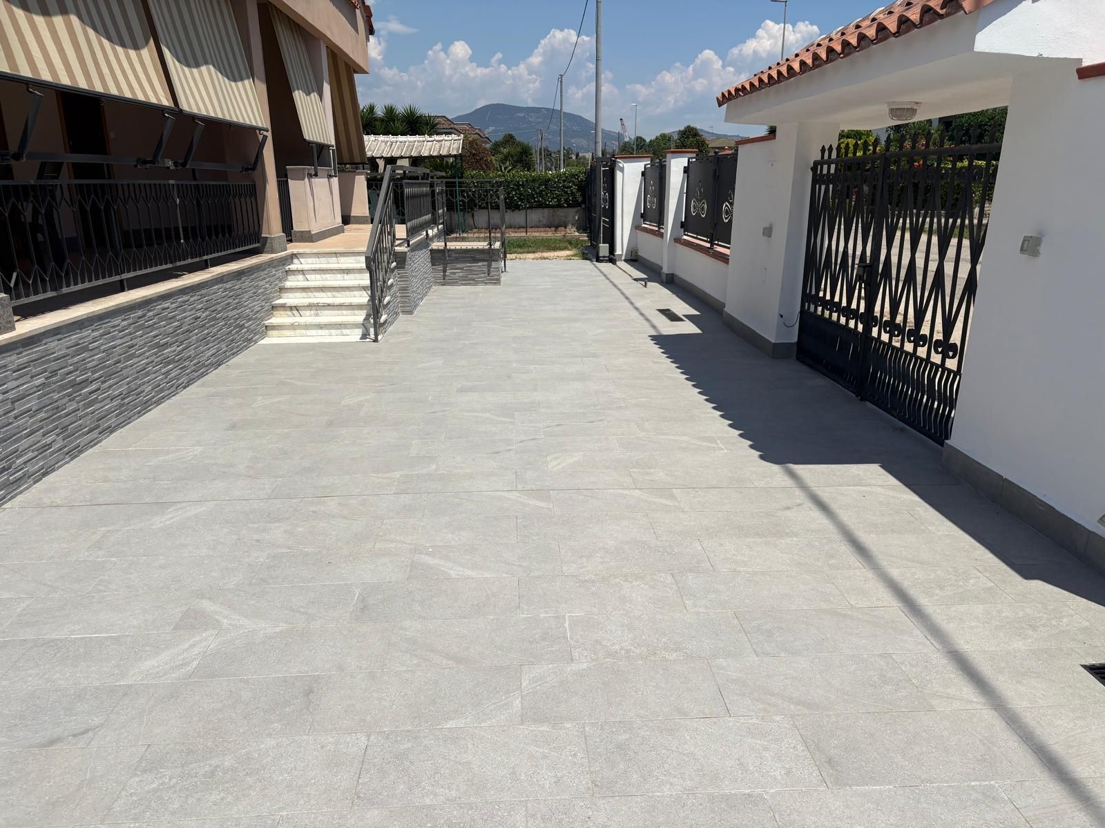 Cortile pavimentato vuoto tra edifici bianchi con ringhiere nere e una vista sulle montagne in lontananza.