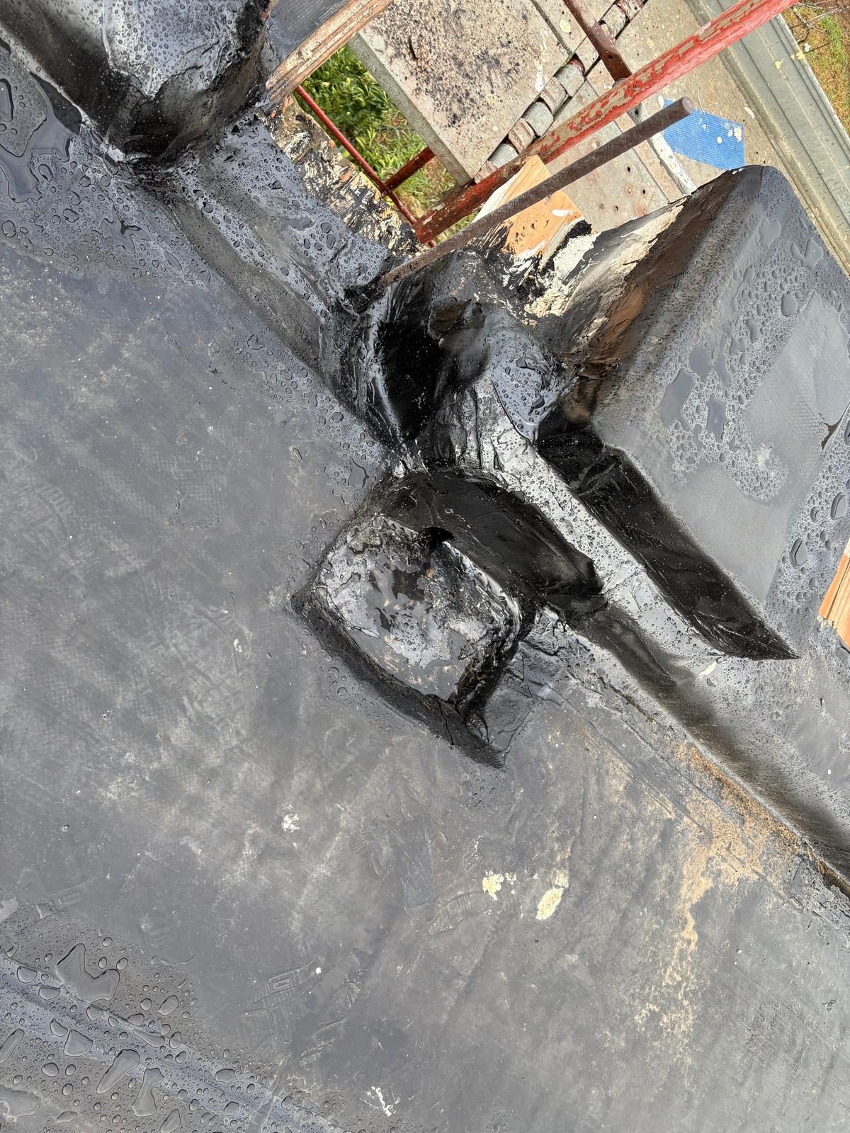 Tetto in cemento con tubo nero, piccola scatola di derivazione e ringhiera rossa addossata al muro di un edificio.