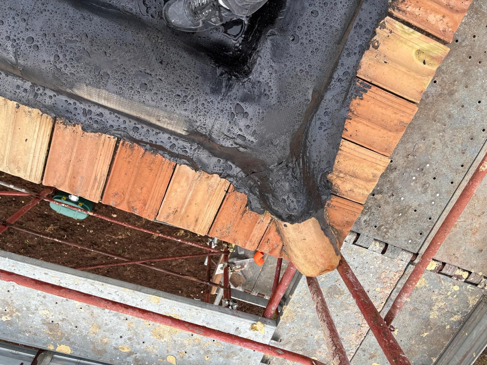 Primo piano del bordo del tetto in mattoni e cemento con l'impermeabilizzazione scura e l'impalcatura metallica sottostante.