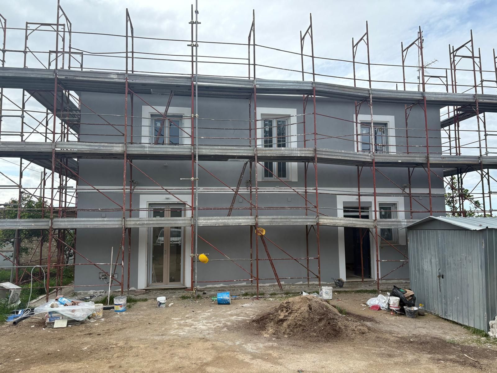 Casa a due piani in costruzione con impalcature e pareti esterne grigie non rifinite.